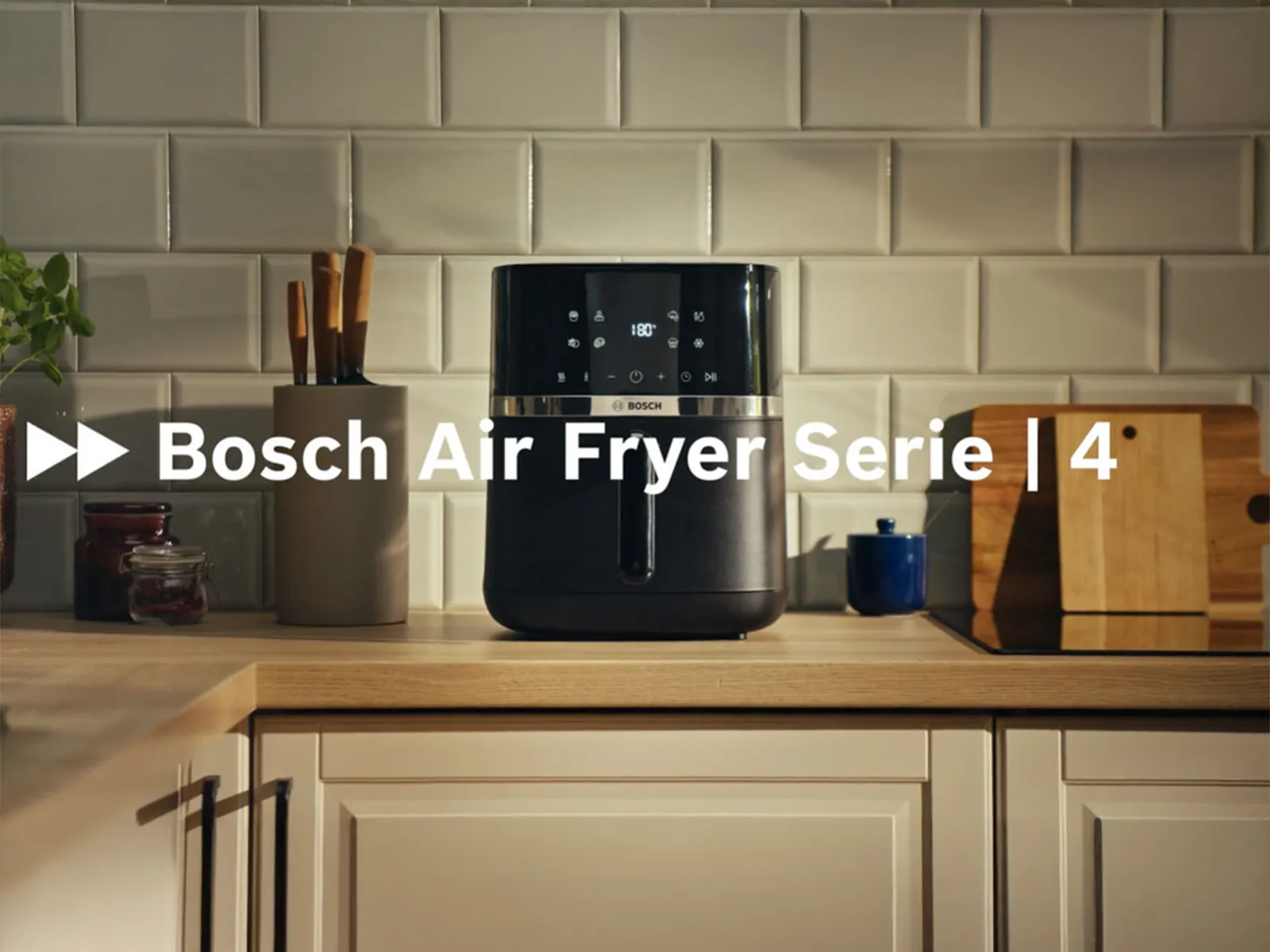 Bosch Air Fryer na kuhinjskoj radnoj površini s otvorenom ladicom, zlatno-smeđa pileća krilca nalaze se u ladici, a uređaj je okružen tanjurima s raznim ukusnim namirnicama kao što su hrskavo pečeno povrće i sočni fileti lososa.
