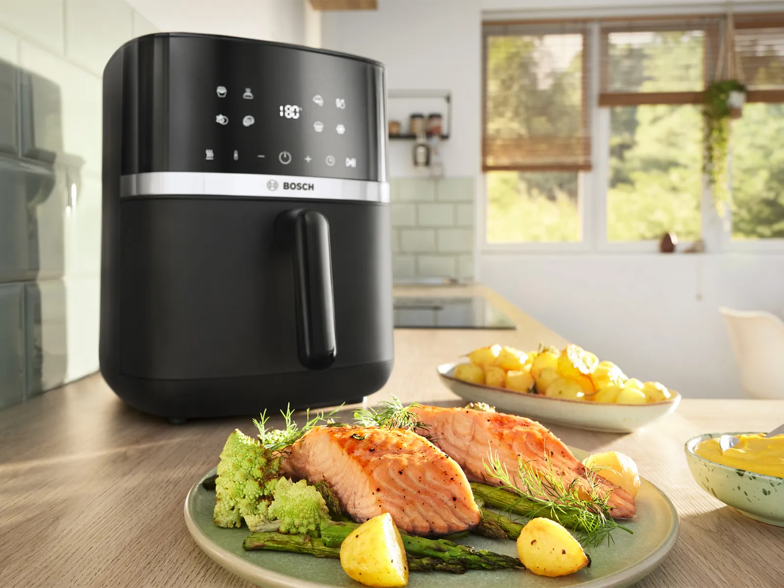 Mətbəx tezgahında yaxınlıqda bir boşqab qızılbalıq, tərəvəz və kartof olan Bosch air fryer.