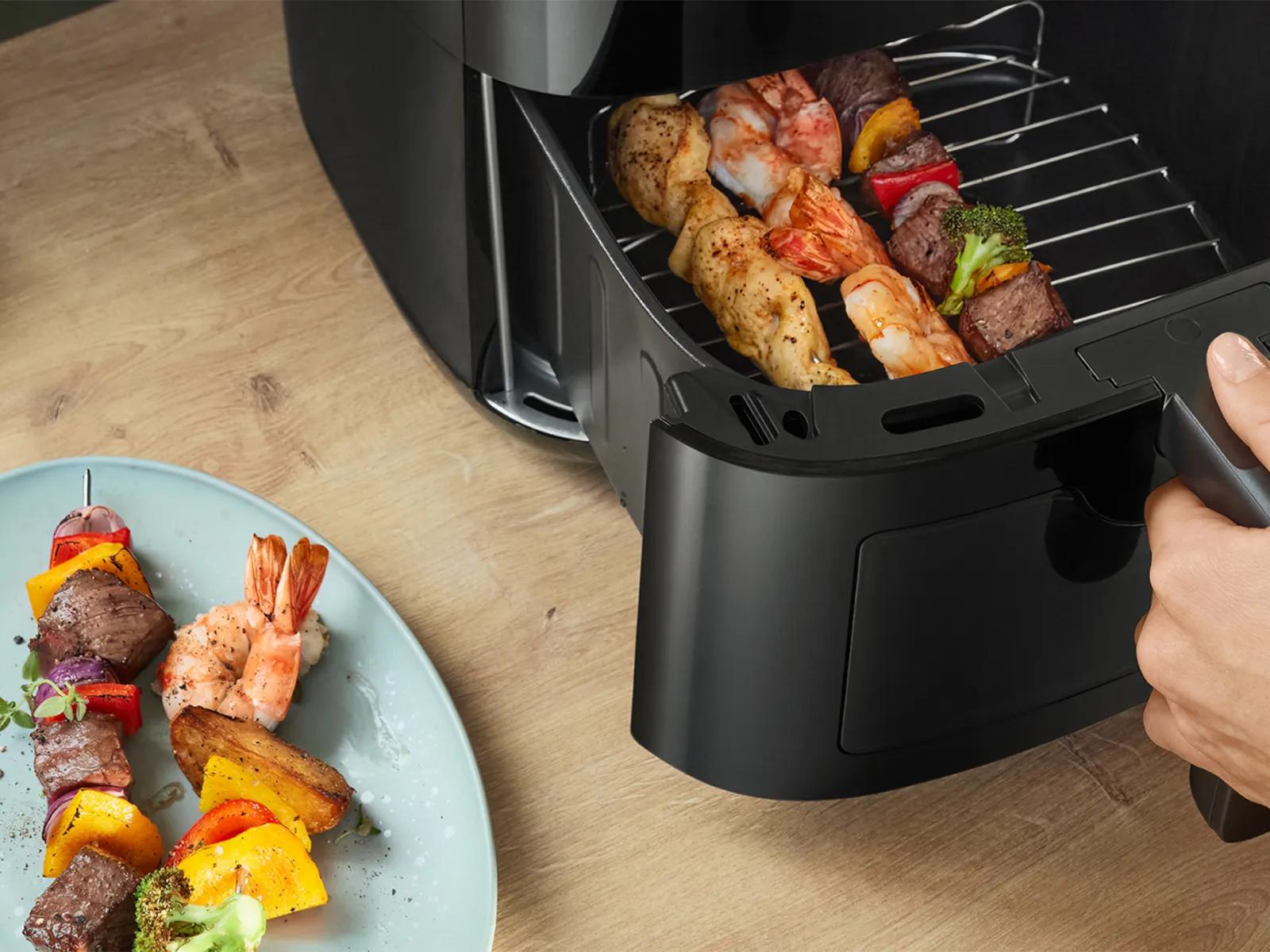 Ένα πιάτο με ζουμερά σουβλάκια με ψητό φιλέτο, γαρίδες και λαχανικά βρίσκεται δίπλα στο ανοιχτό συρτάρι ενός φούρνου αέρα Bosch.
