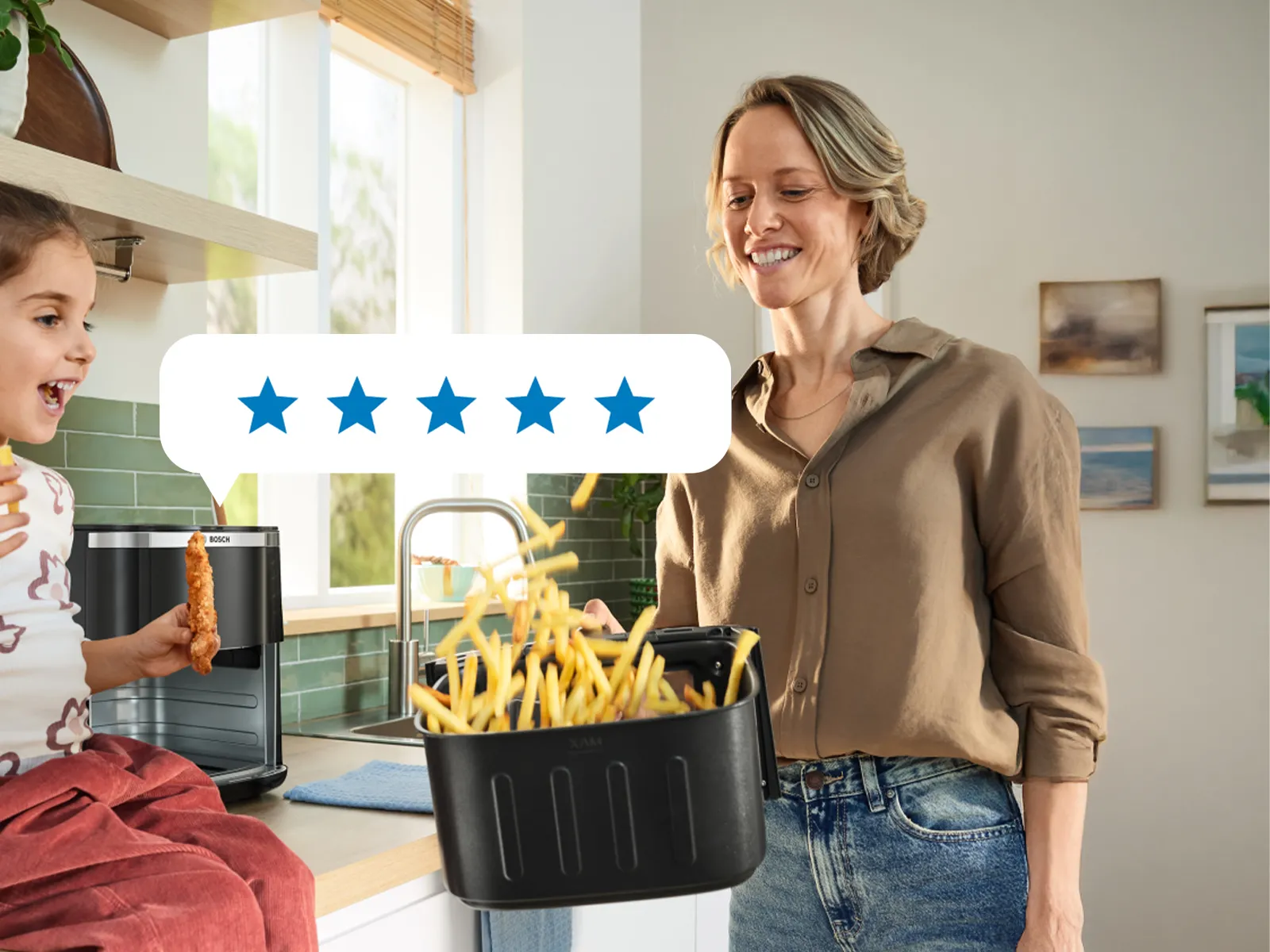 A mother shakes the basket of a Bosch Air Fryer while her daughter sits on the kitchen counter, smiling and enjoying the cooking process together.