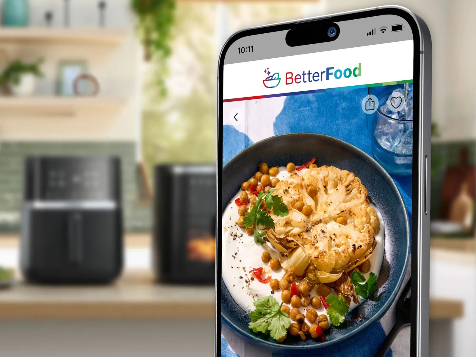 On the screen of a mobile phone the Bosch better food App is shown. In the background a kitchen counter with  Bosch Air fryers.