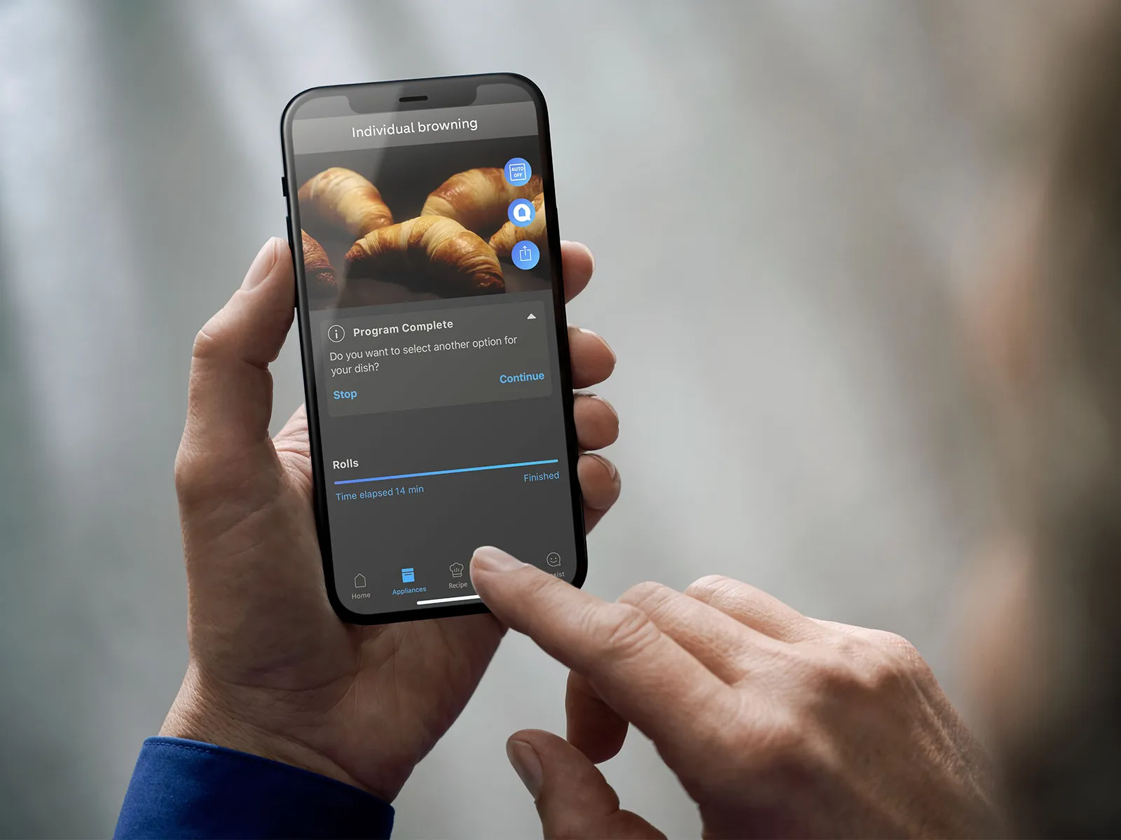 A hand holding a smartphone displays a cooking app screen showing completed browning for rolls, with timer details visible.