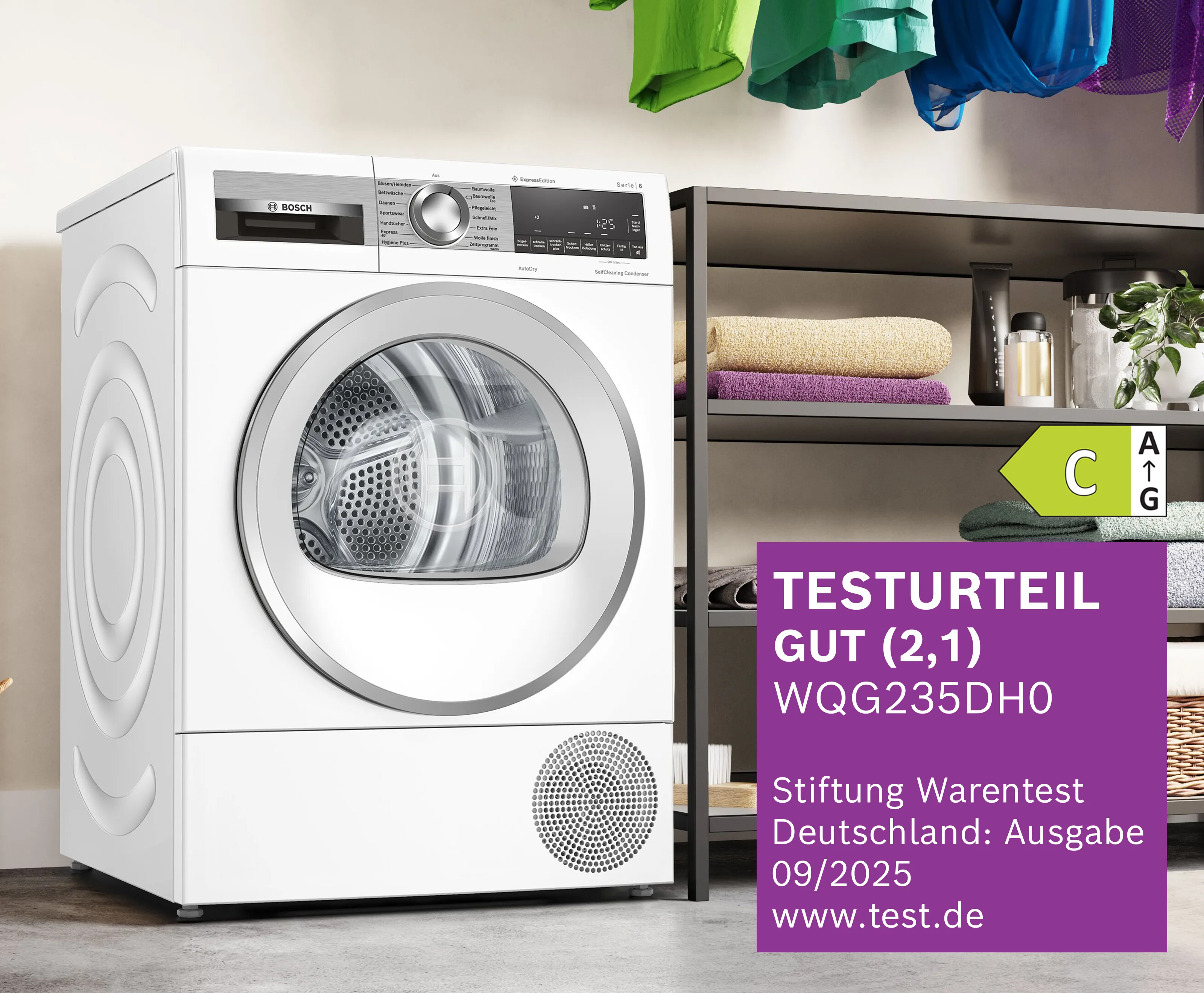 Ein moderner weißer Trockner mit transparenter Tür steht neben ordentlich gefalteten Handtüchern auf einem Regal und zeigt ein Energieeffizienzlabel.