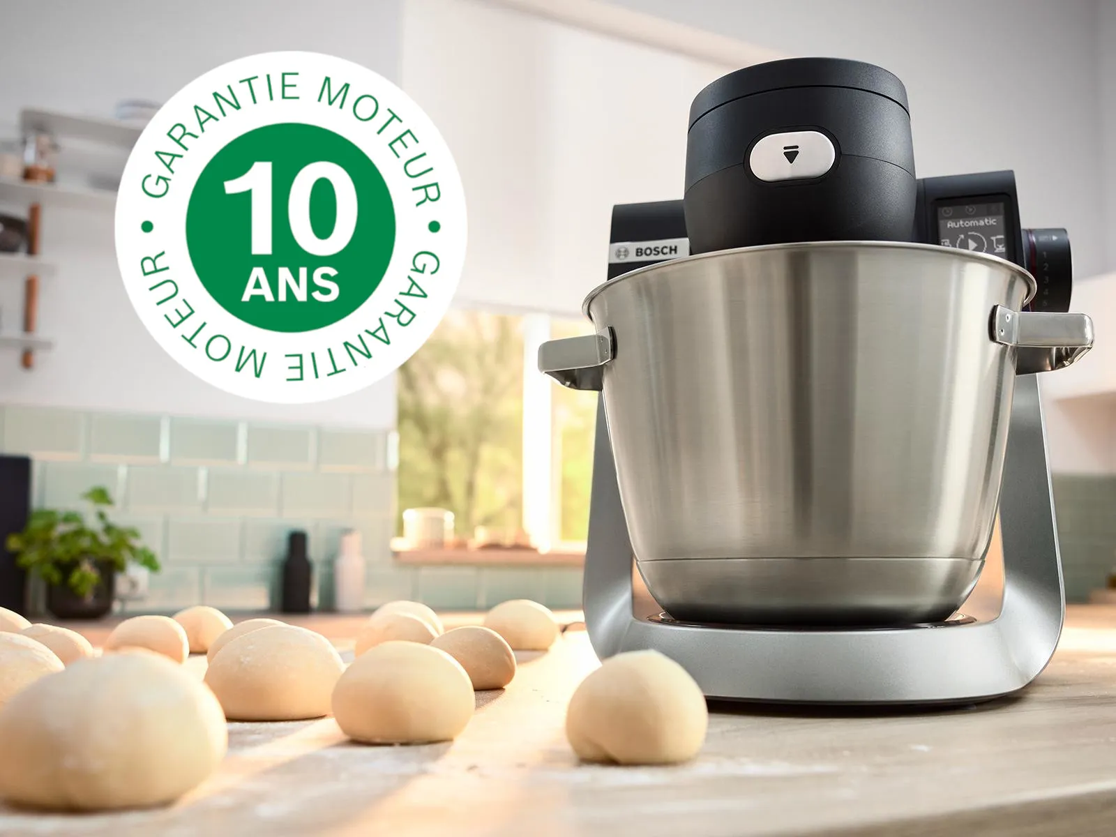 L'image montre le robot pâtissier Série 6 sur le plan de travail de la cuisine à côté de plusieurs boules de pâte et du logo de garantie de 10 ans superposé.