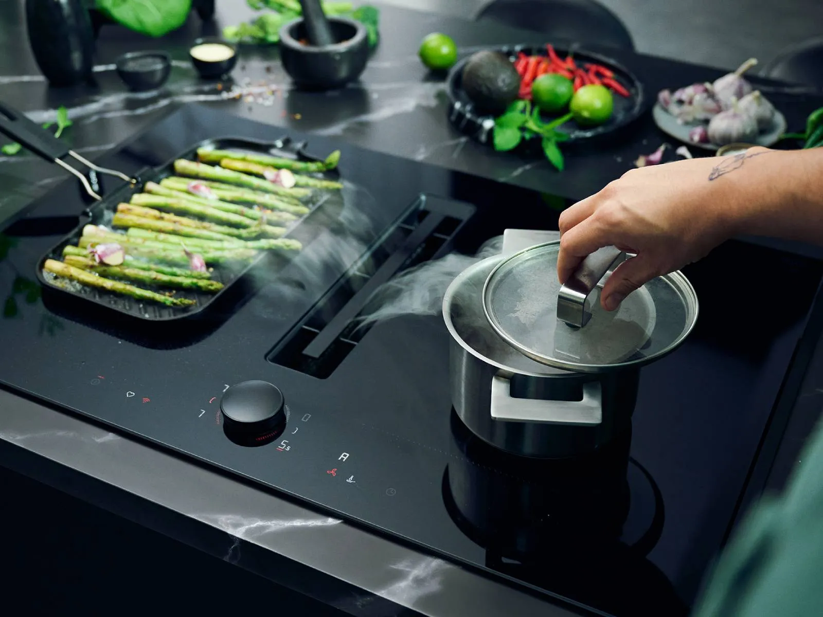 A person cooks asparagus on a vented hob, focusing on the vibrant green vegetables in a frying pan.  