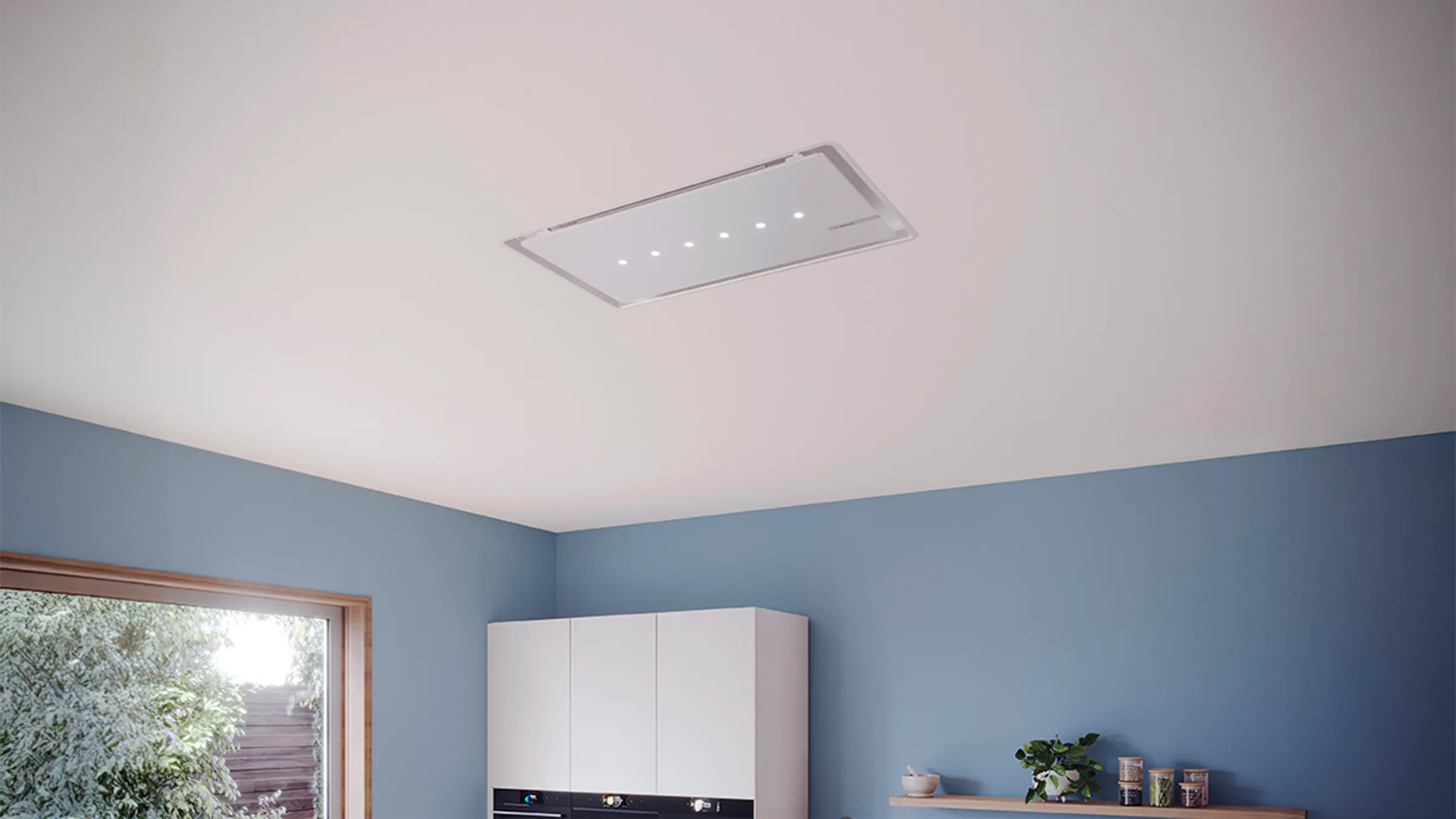 Ceiling-mounted kitchen hood integrated into a modern kitchen with blue walls and white cabinets.