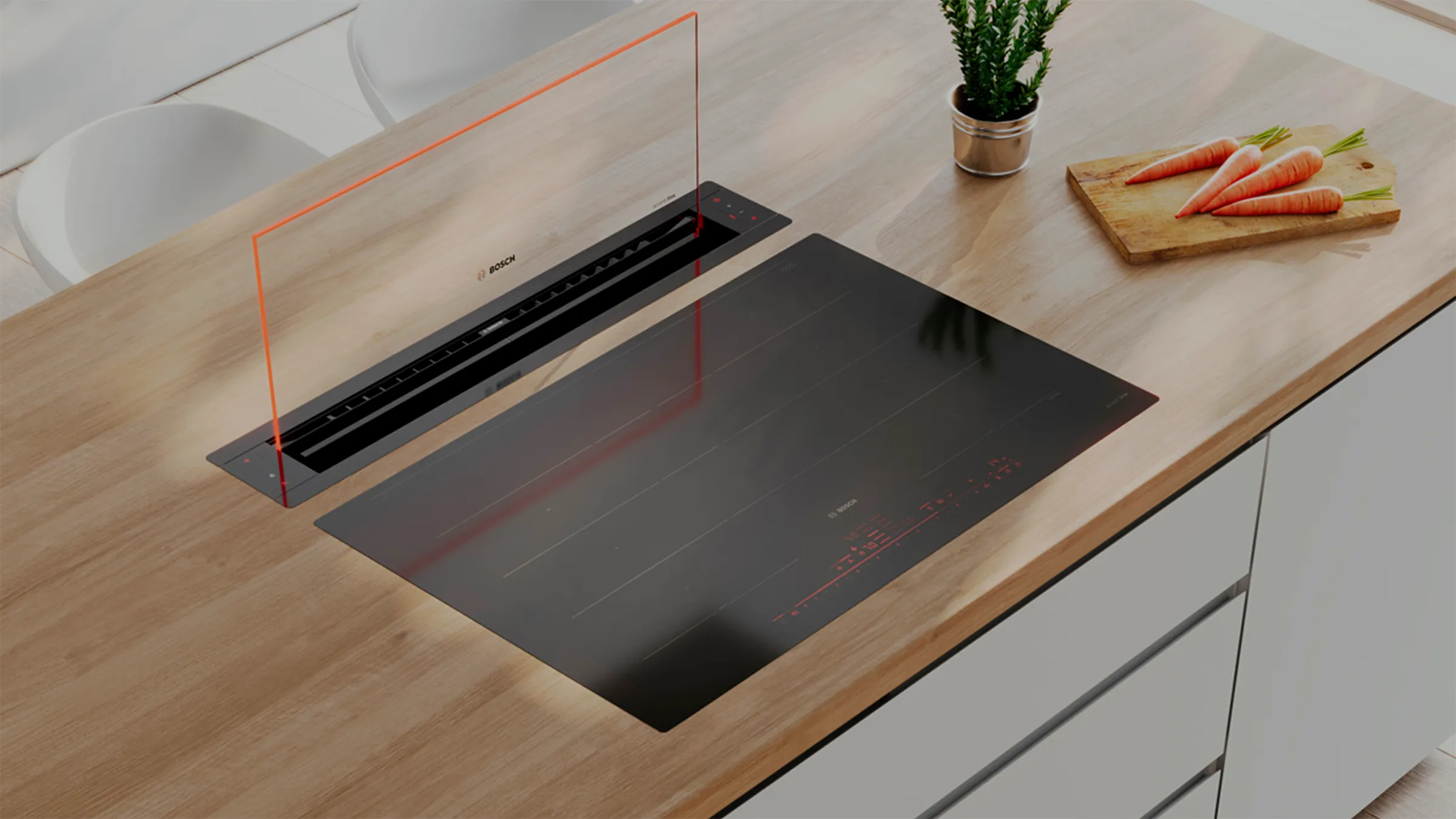 Cooktop with integrated downdraft vent on a wooden counter, with a plant and carrots nearby.