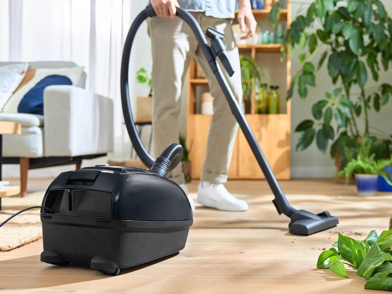 Person vacuuming wooden floor with bagged vacuum.