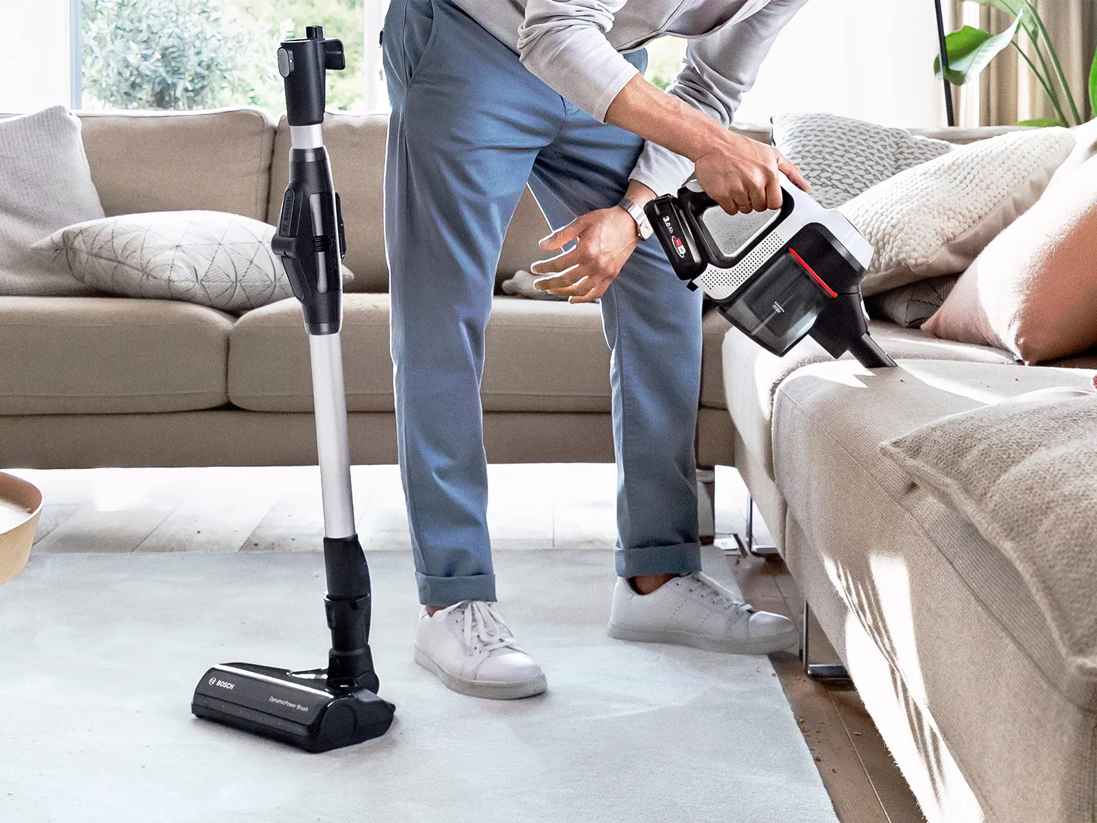 Person using Bosch vacuum cleaner hand-held feature to clean a sofa.