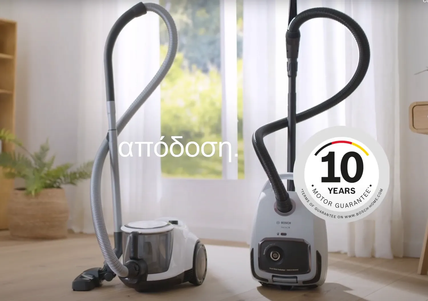 Δύο κυλινδρικοί σκουπάκοι Bosch χωρίς σακούλα στέκονται μπροστά από ένα παράθυρο σε μια μελέτη με τις λέξεις “απόδοση για όλες τις επιφάνειες” επάνω τους.