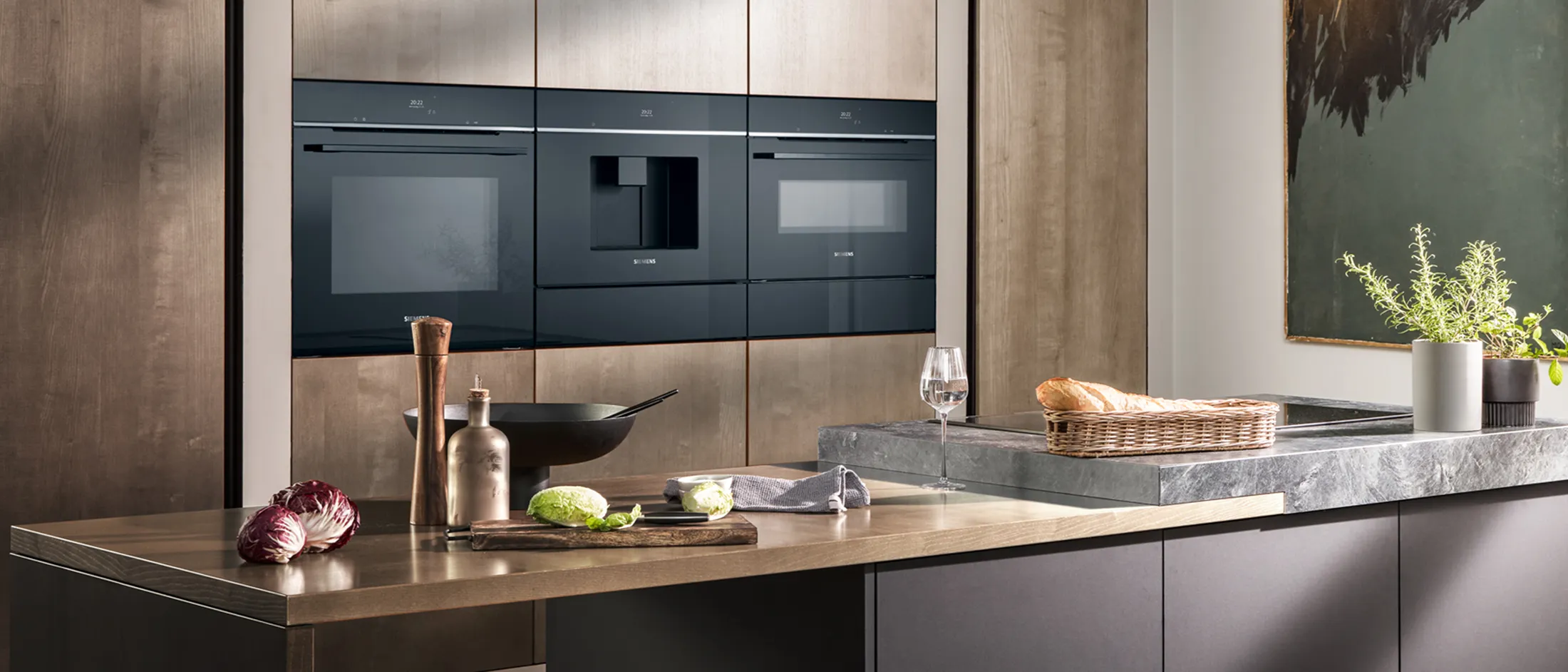 Modern kitchen with sleek black Siemens appliances mounted on a ribbed wood wall, featuring a dark marble countertop and greenery.