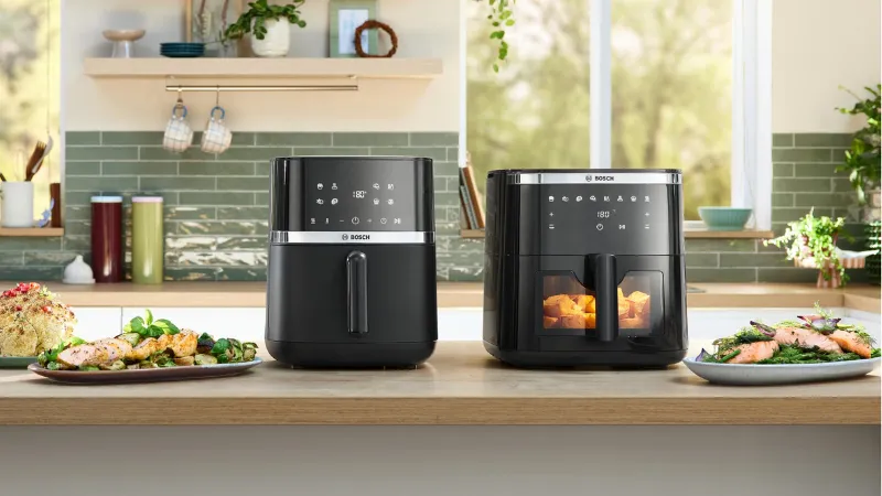 Una elegante freidora de aire Bosch negra, con una ventana transparente que muestra la comida en su interior y controles digitales en el panel superior.