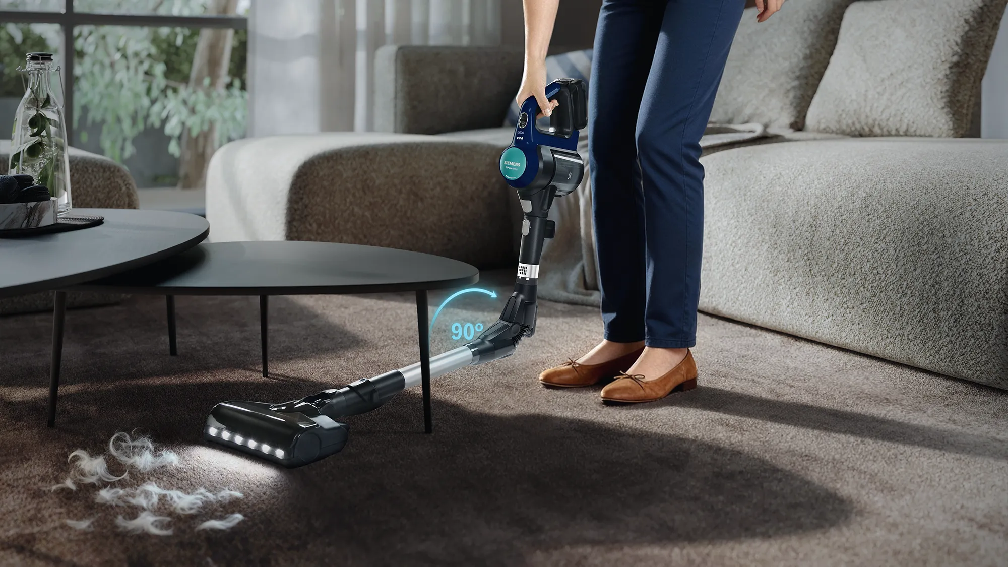 A person using a cordless vacuum cleaner to clean a carpet, with a graphic showing 90-degree maneuverability.