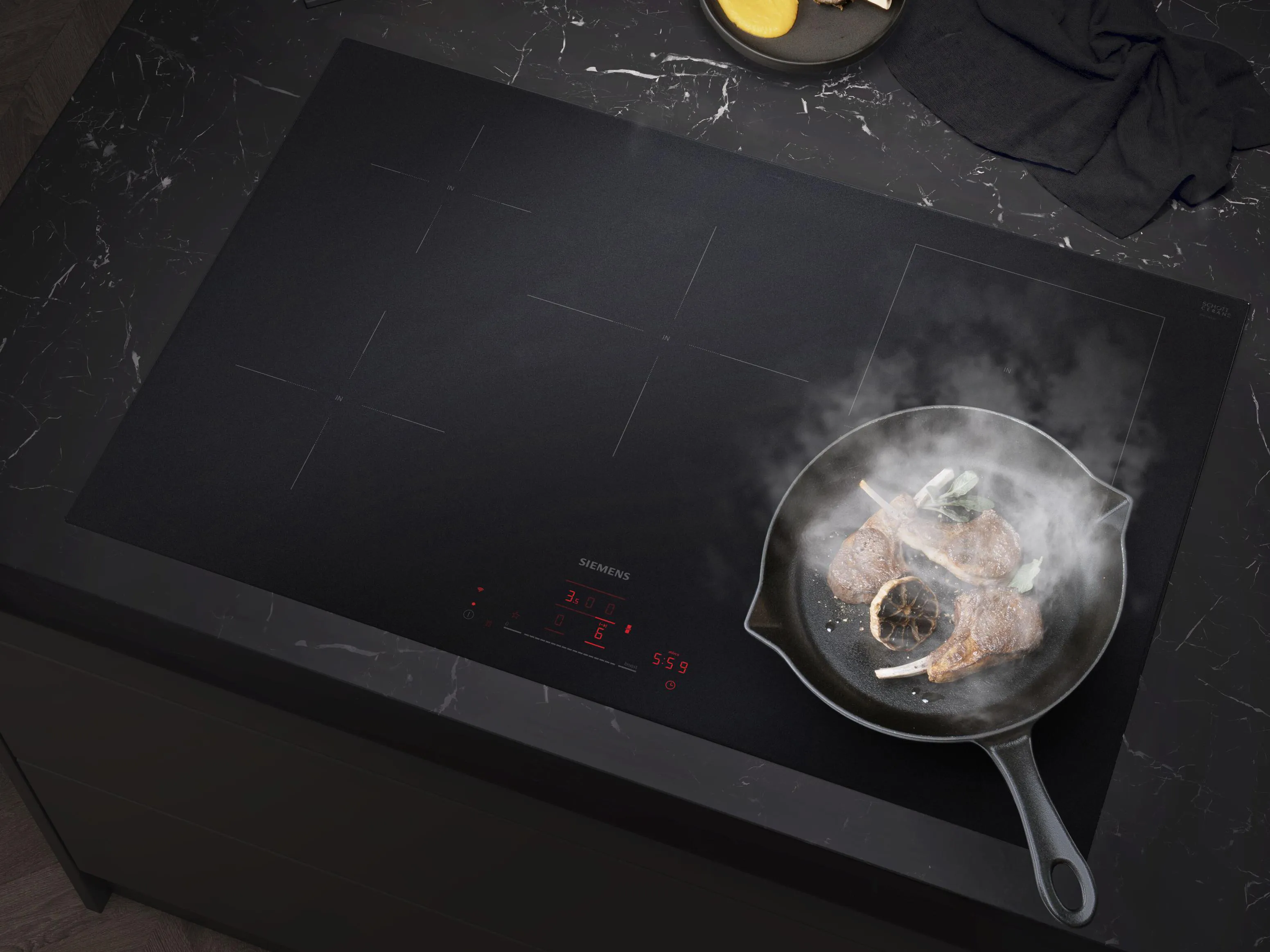 Skwierczące mięso na czarnej płycie indukcyjnej, w towarzystwie świeżych cytryn i stylowego marmurowego blatu