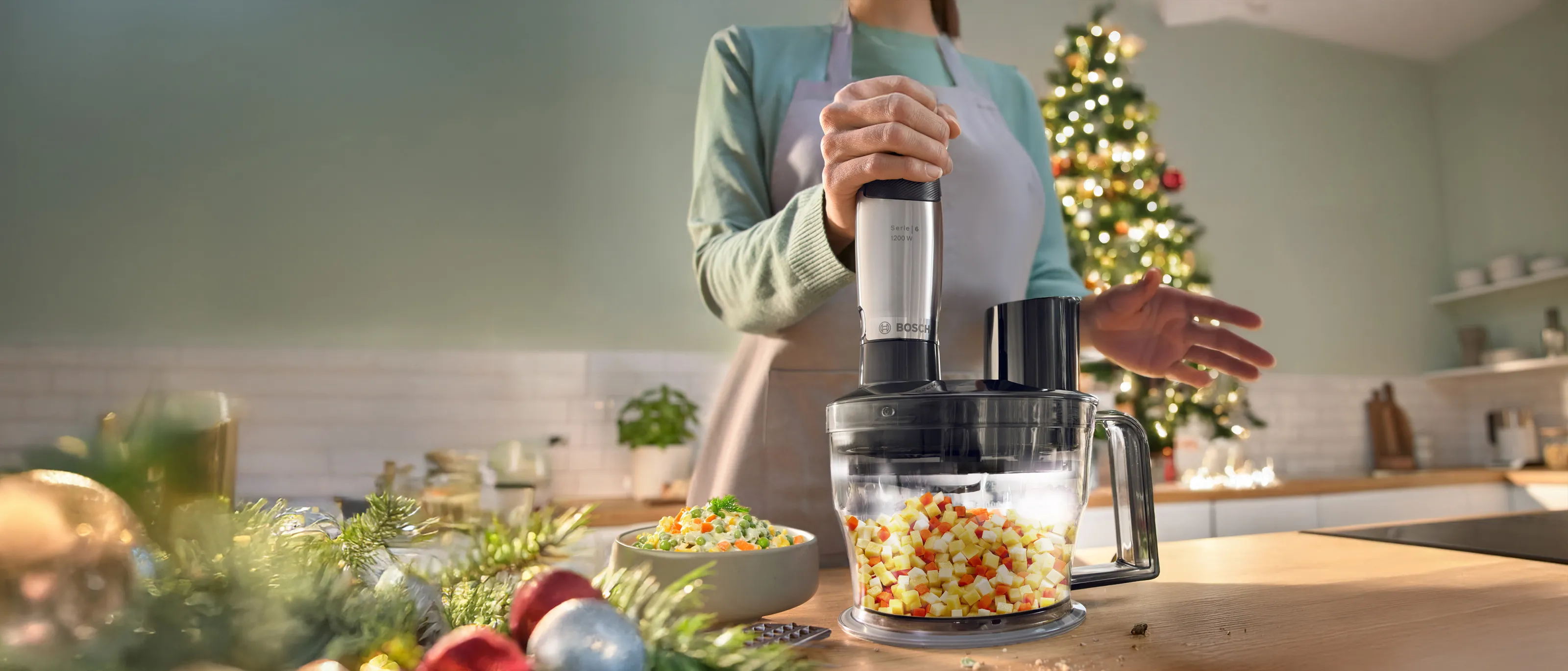 Kobieta w filotowym dresie, w kuchni przy blacie, trzyma blender ręczny