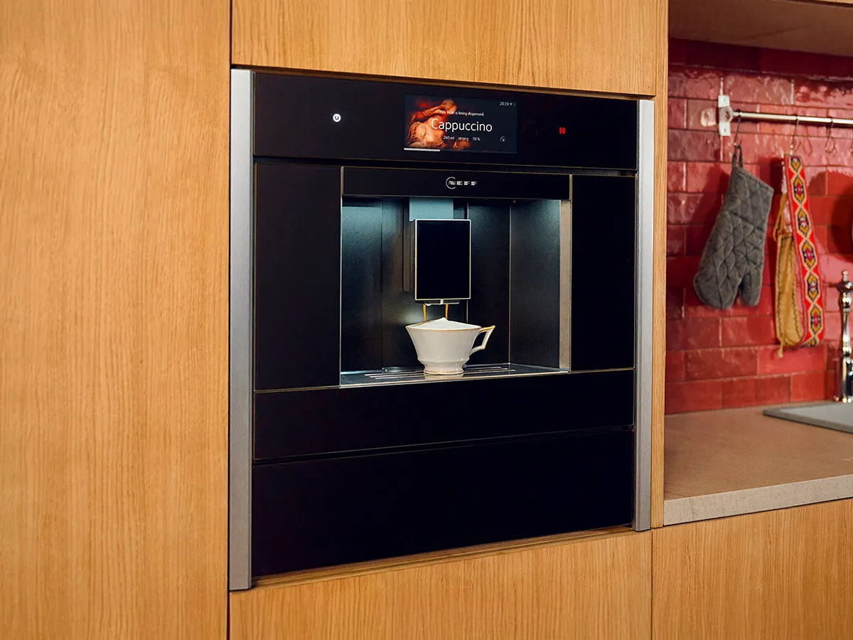 A NEFF coffee machine with silver trims, seamlessly fitted within a kitchen cabinet.