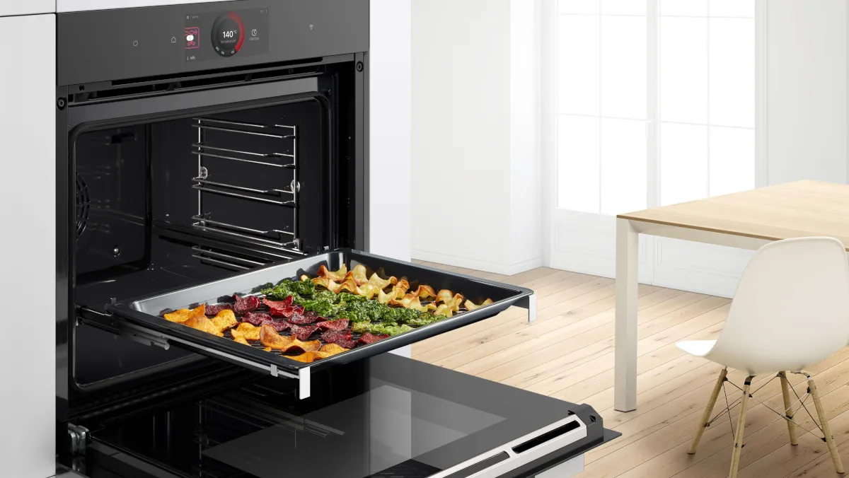 Offener Bosch Serie 8 Backofen mit herausgezogenem Air-Fry-Blech, belegt mit Gemüsechips; Darstellung der Air Fry Funktion für fettarmes, knuspriges Garen im Backofen.