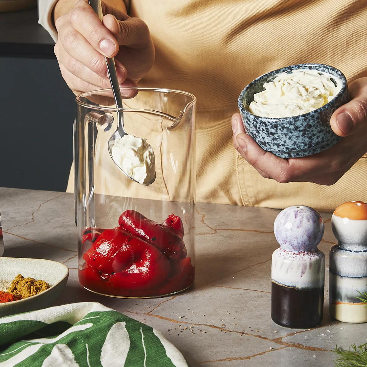 Spooning yogurt into a glass jar filled with roasted red bell peppers