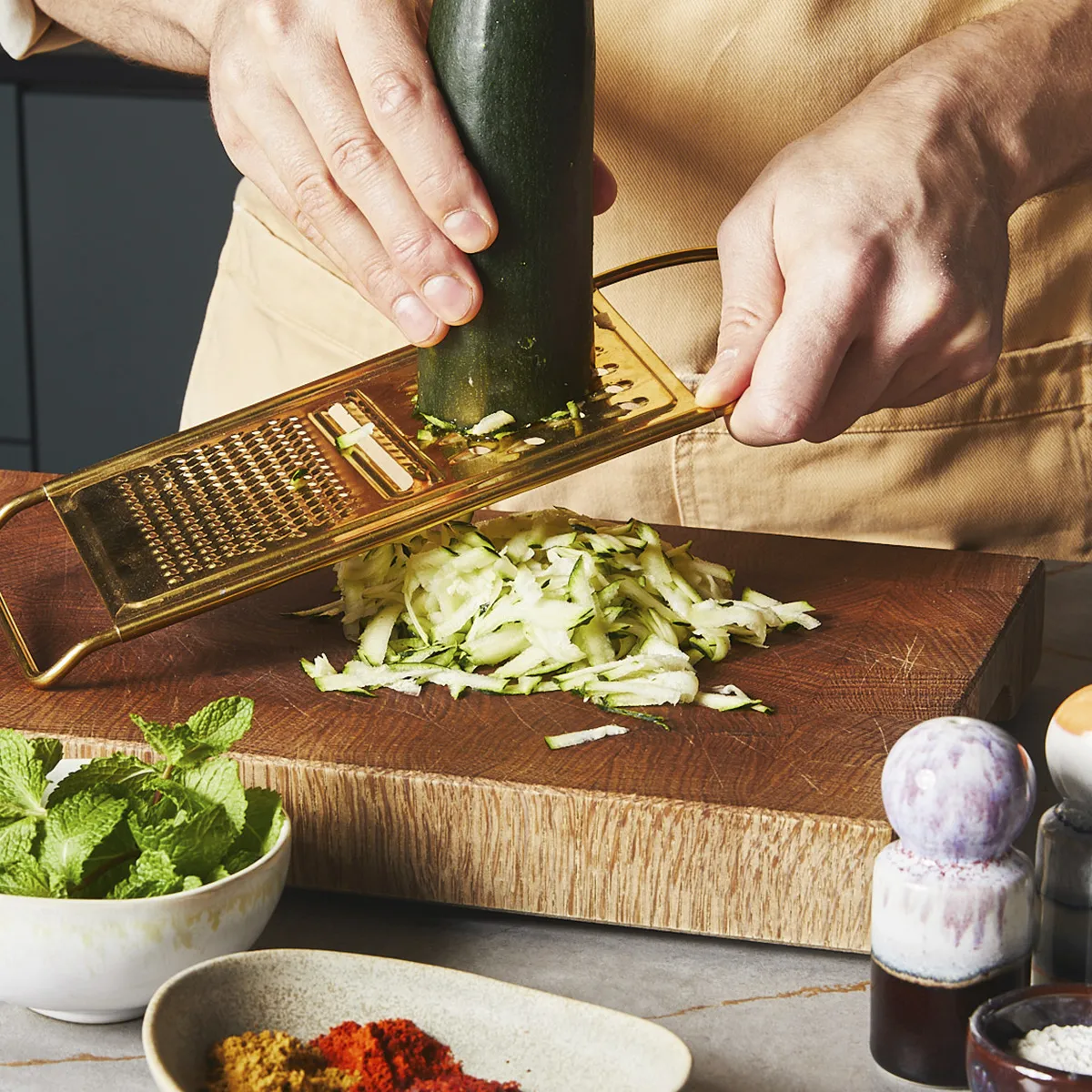 Grating a zucchini with a golden grater on a wooden board