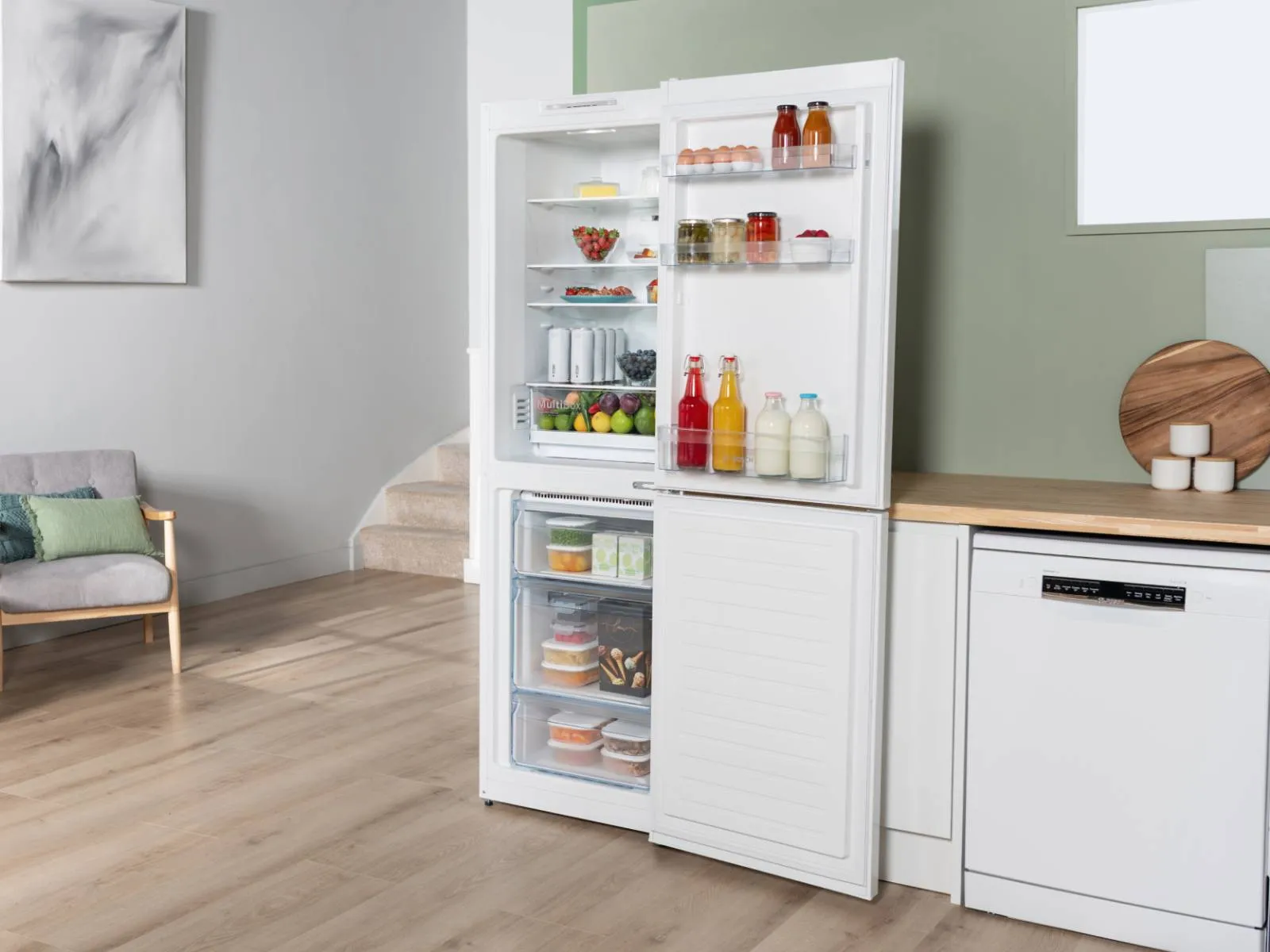 A white Bosch fridge-freezer with its doors open, revealing a fully stocked interior with food and drinks, integrated into a modern kitchen with light wooden countertops and a dishwasher.