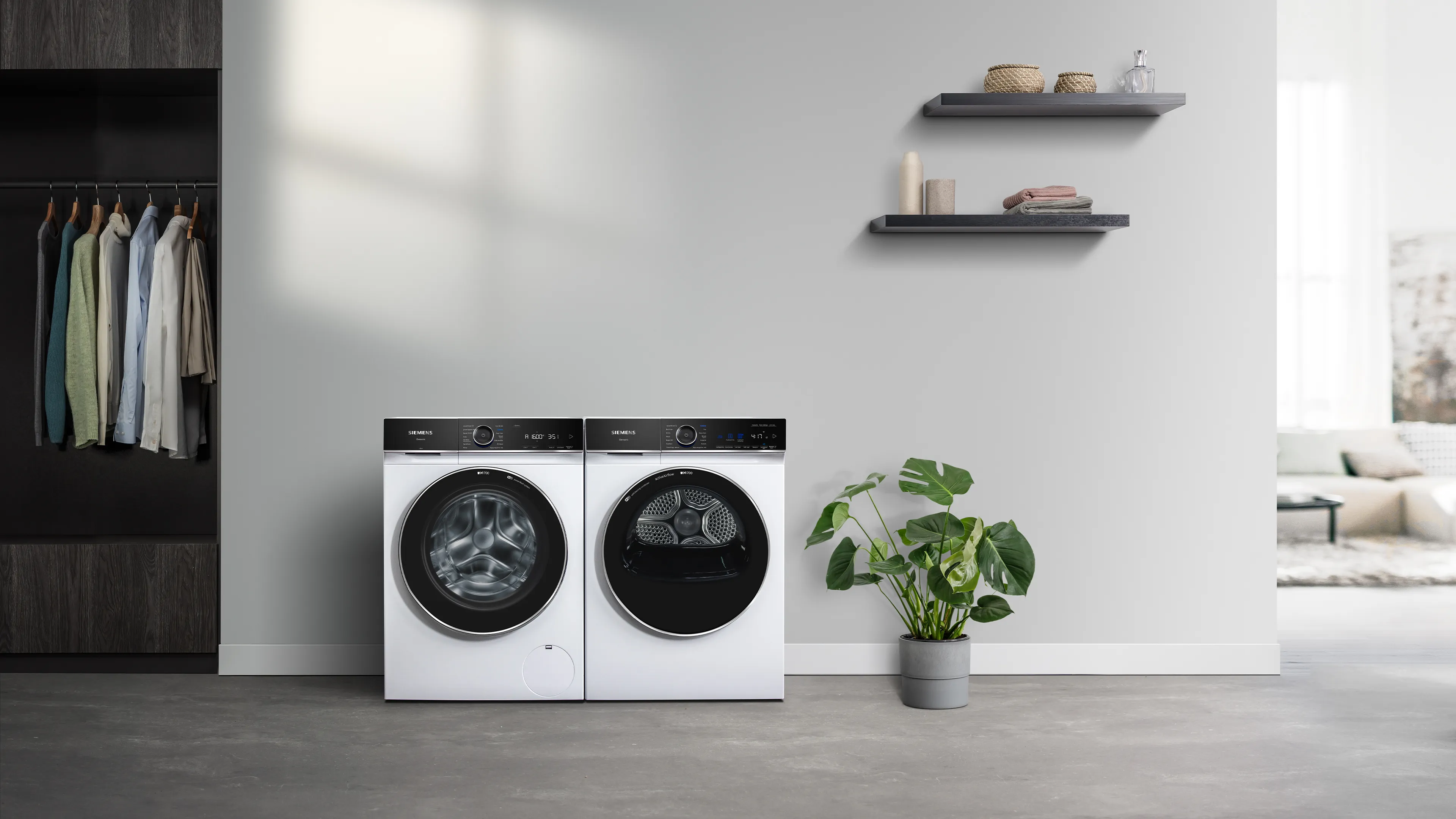 A modern laundry room with a white Siemens washing machine and dryer side-by-side, a closet, and decorative shelves.