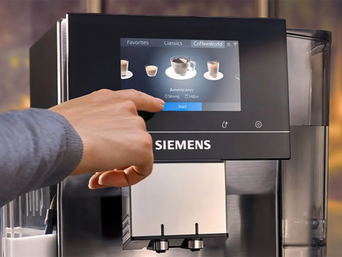 A person's finger selects "Americano" from the large, intuitive touchscreen of a Siemens coffee machine, demonstrating the iSelect Display.