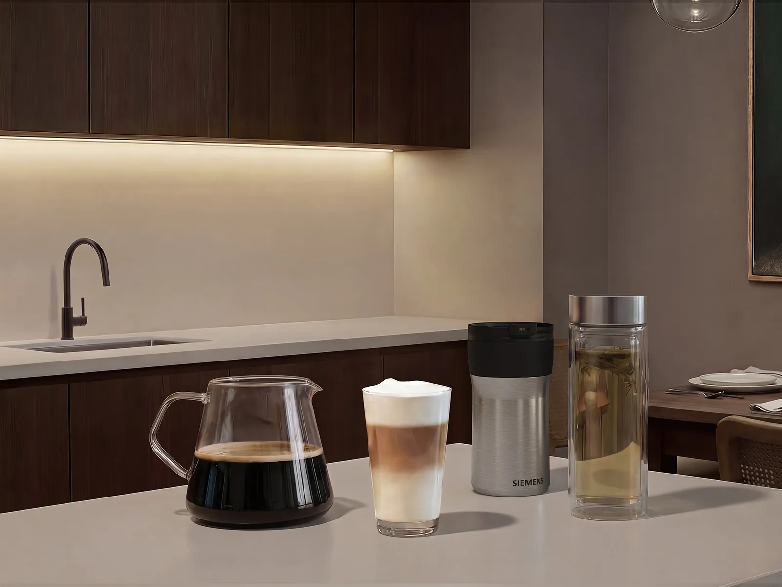 Glass coffee carafe, layered espresso‑and‑milk drink, Siemens stainless travel mug, and glass tea infuser arranged on a light, minimalist kitchen countertop.