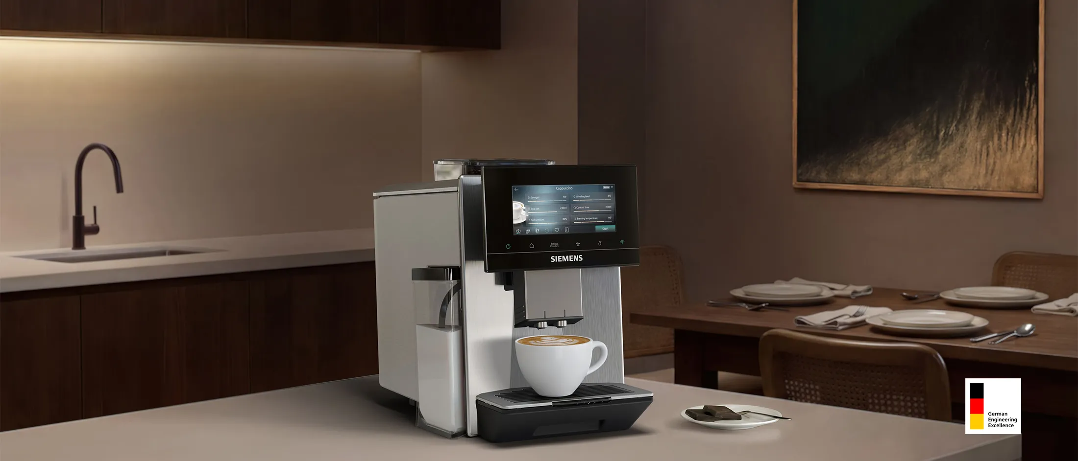 Siemens coffee machine with touchscreen and ready cappuccino in white cup: warm, softly lit kitchen in the background with dark cabinets, a small plant, and a set dining table with wine and candlelight.
