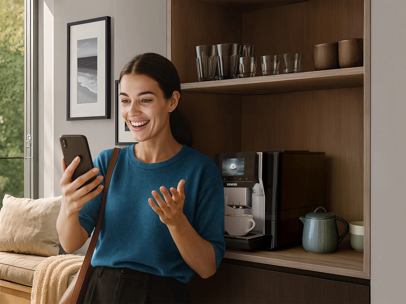 Woman in a bright, modern room smiling at her smartphone; wooden shelf with glasses, brown cups, and a light blue teapot; Siemens coffee machine in the corner; large windows, beige couch with throw, and framed seascape on the wall.