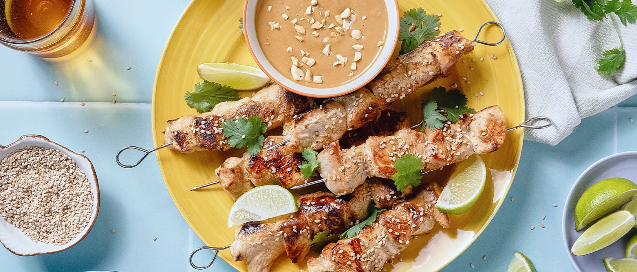 Spiedini di pollo fritto su un piatto giallo, accanto a una ciotola piena di salsa marrone. 