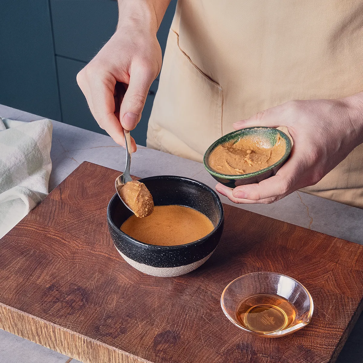 A hand gives a spoon full of peanut butter into a bowl half filled with liquid.