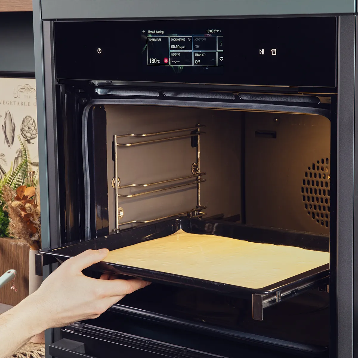 A hand transfers a baking tray with dough spread out on it to an oven