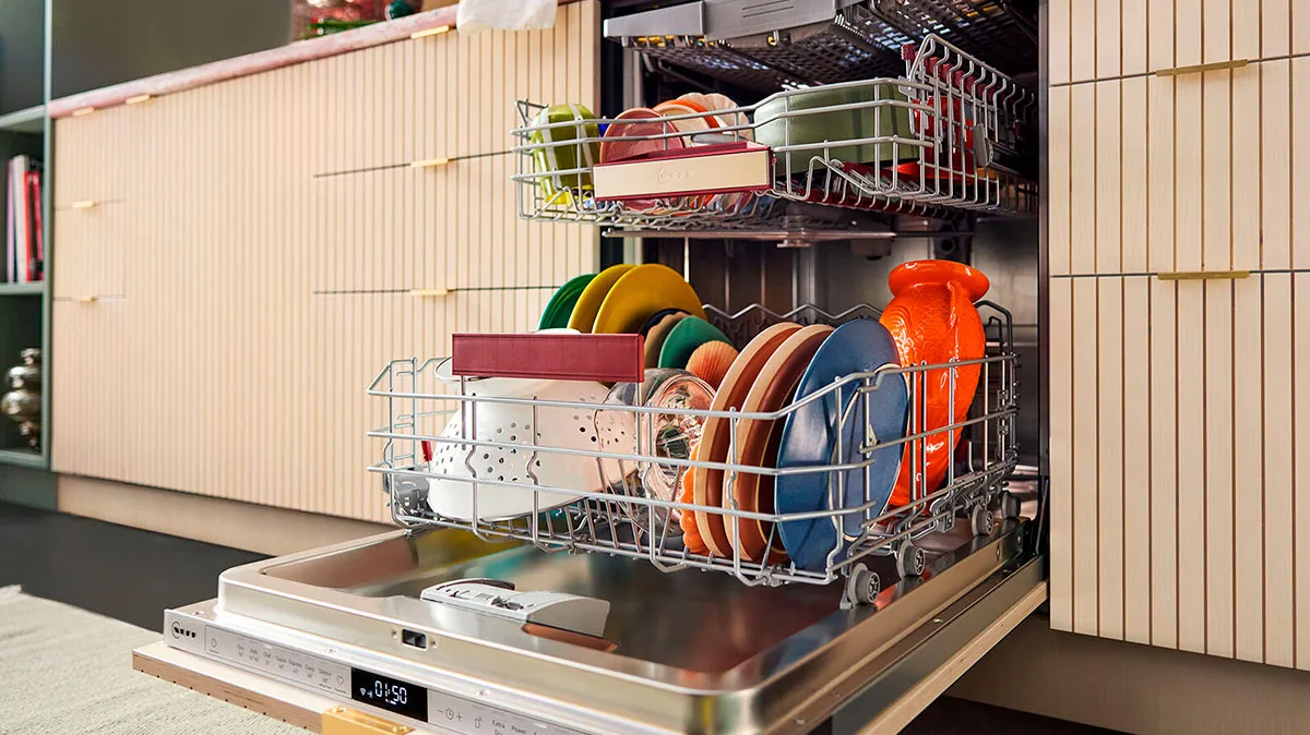 Moderne opvaskemaskine med farverige tallerkener og åben låge, indbygget i et stilfuldt træ-køkken.