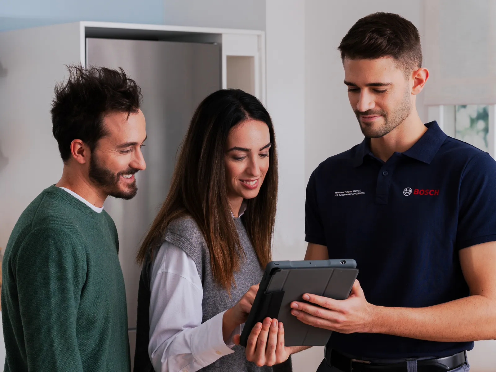 Bosch employee showing information on a tablet to a smiling couple in a modern home.