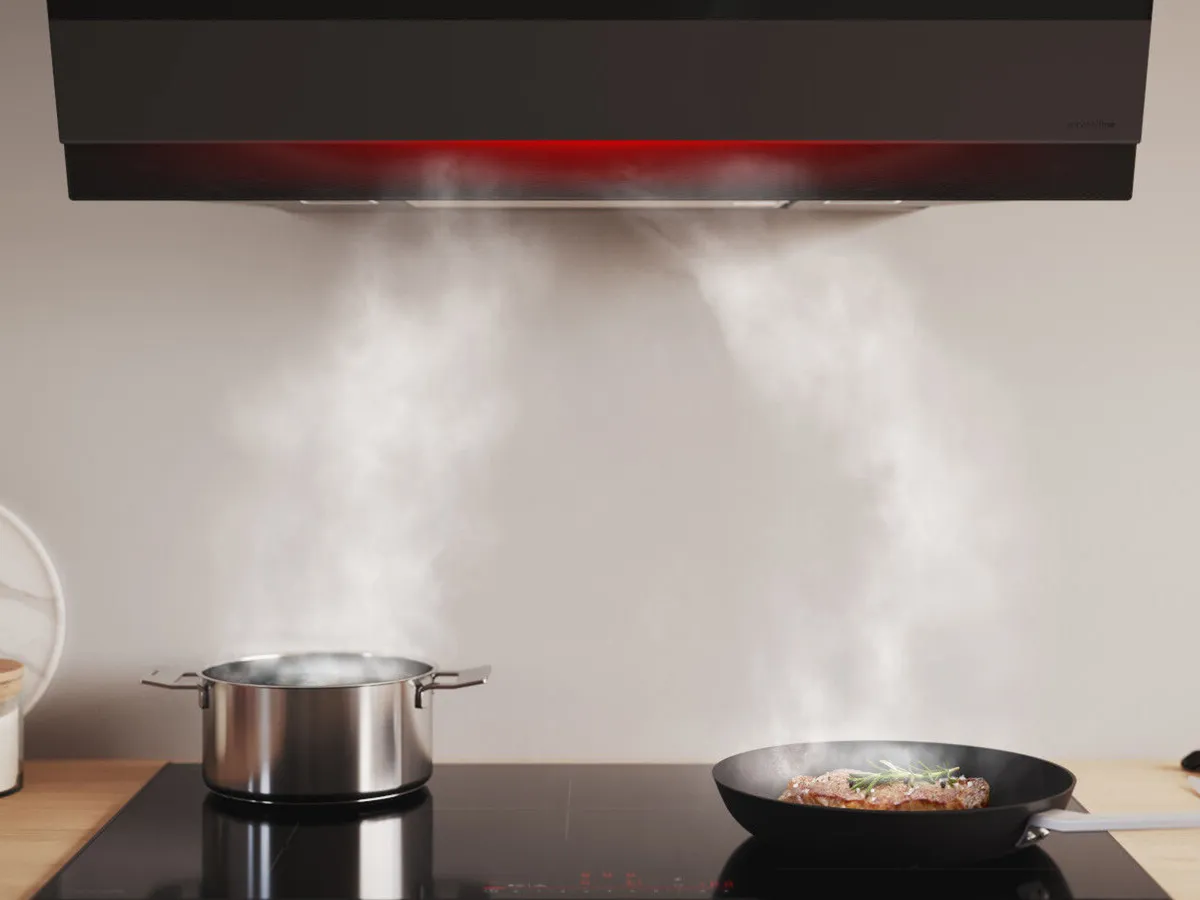 Black wall-mounted canopy rangehood atop an induction cooktop with pots and pans.