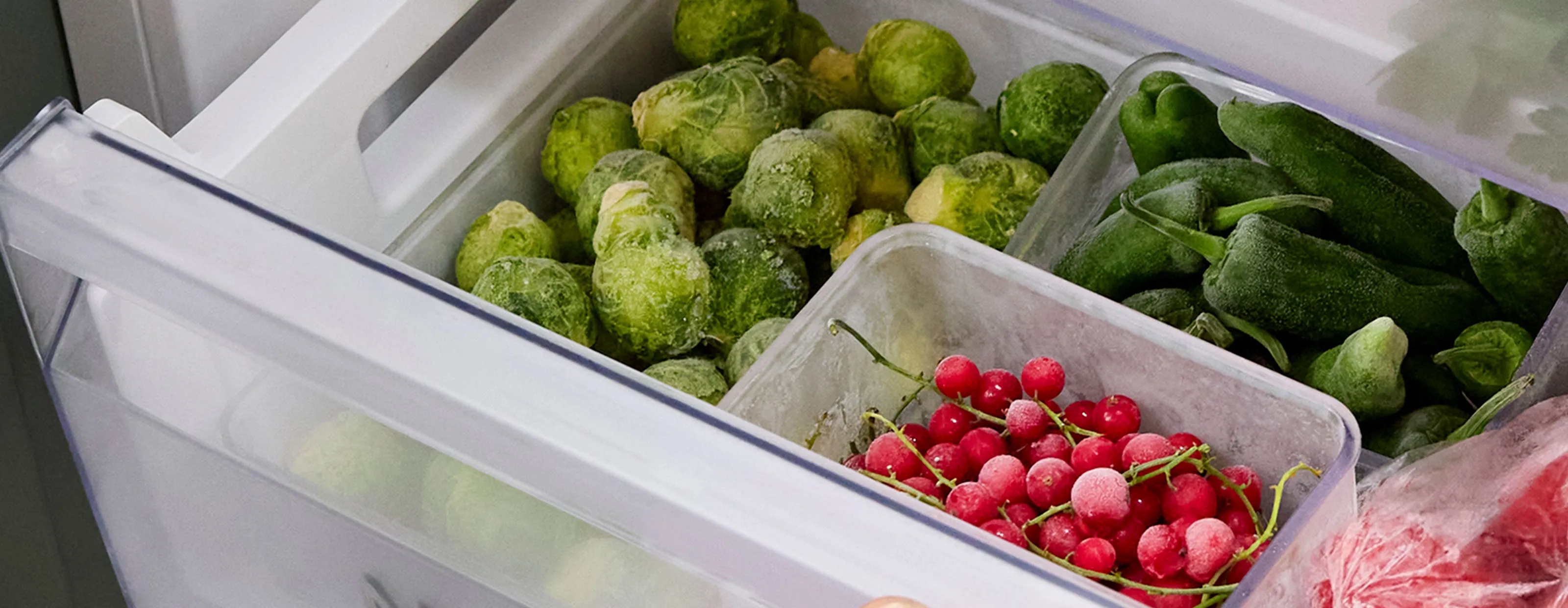 En hand öppnar en fryslåda fylld med frysta matvaror, frysen har NoFrost.