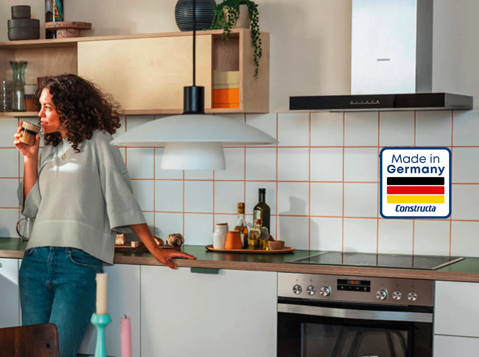 Eine Frau trinkt Kaffee in einer modernen Küche mit Constructa Geräten. Mit "Made in Germany" Label.