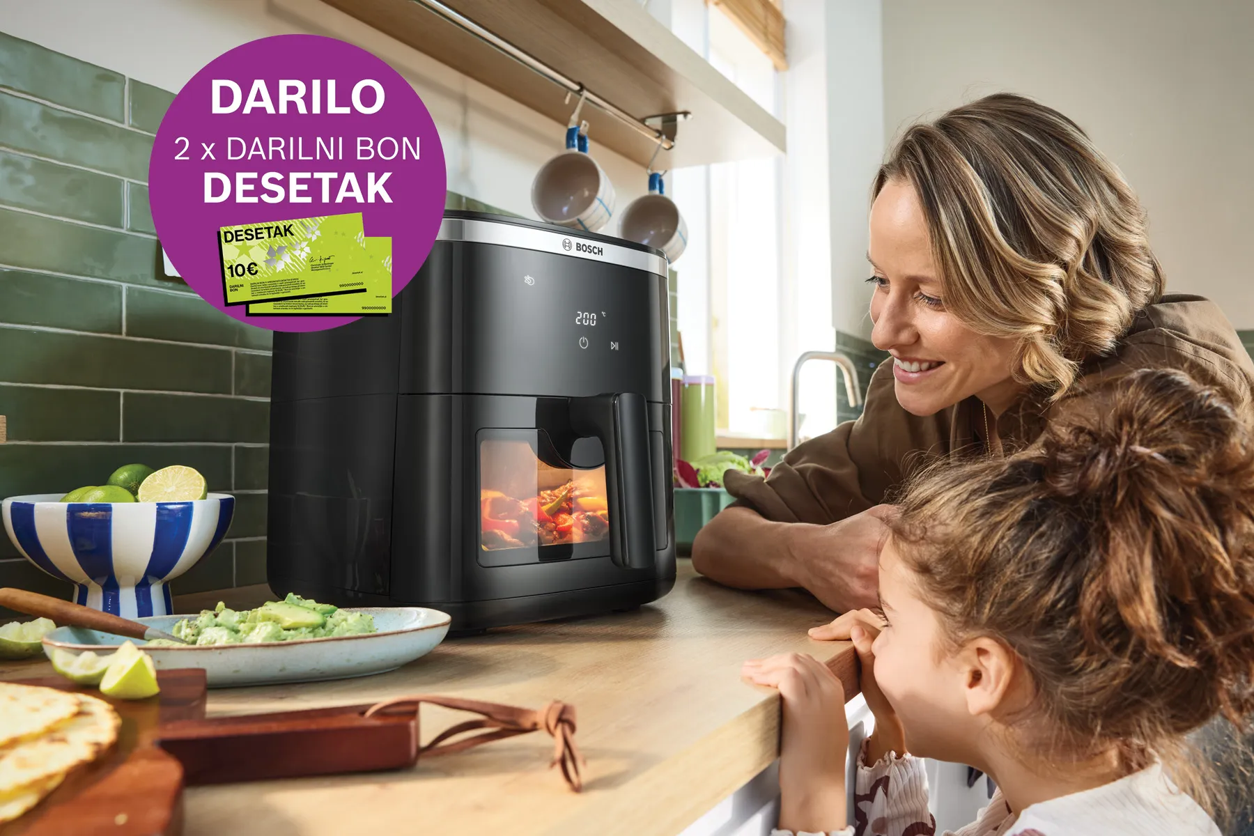 Dva otroka opazujeta črno fritezo na kuhinjskem pultu, ob njej pa so krožniki in jedilni pribor