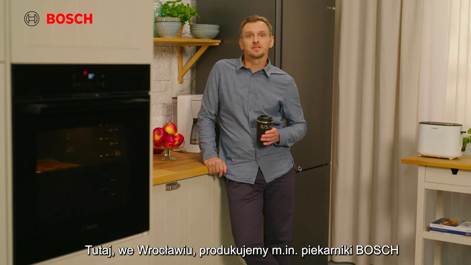 Mezczyzna stoi w kuchni, w zabudowie jest pierkanik, obok lodowka i stol