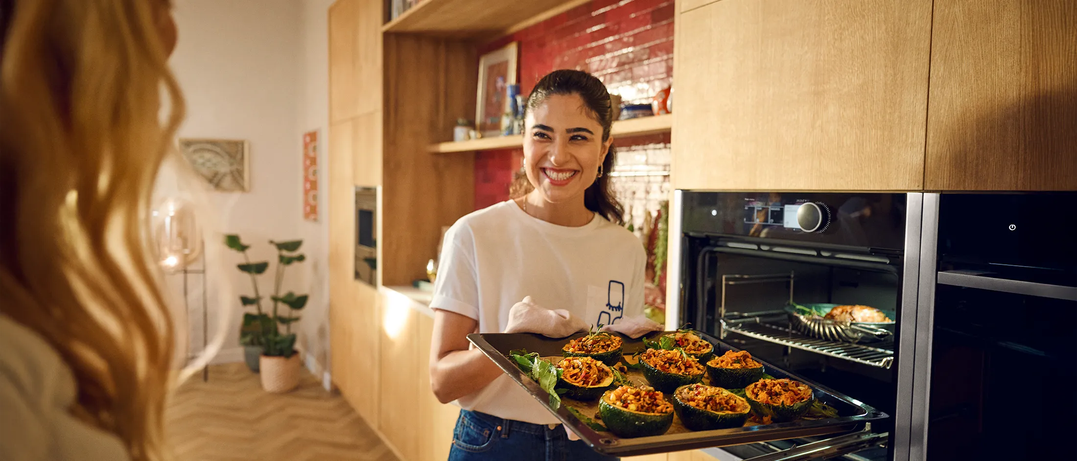 Una persona in una cucina moderna, tiene un bicchiere e indossa una camicia bianca con un asciugamano colorato sulle spalle. Sulla destra il logo "Cashback 300€"