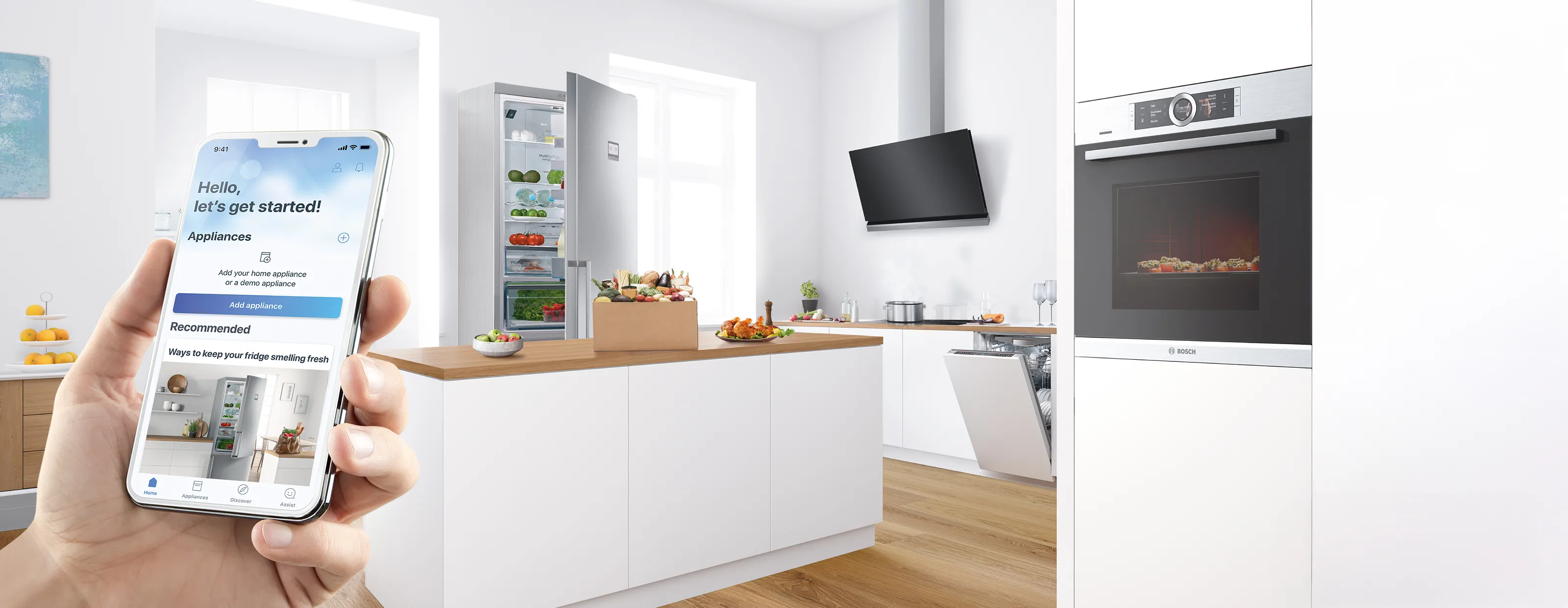 Hand holding smartphone with smart appliance app in modern kitchen featuring open fridge, oven, and dishwasher.