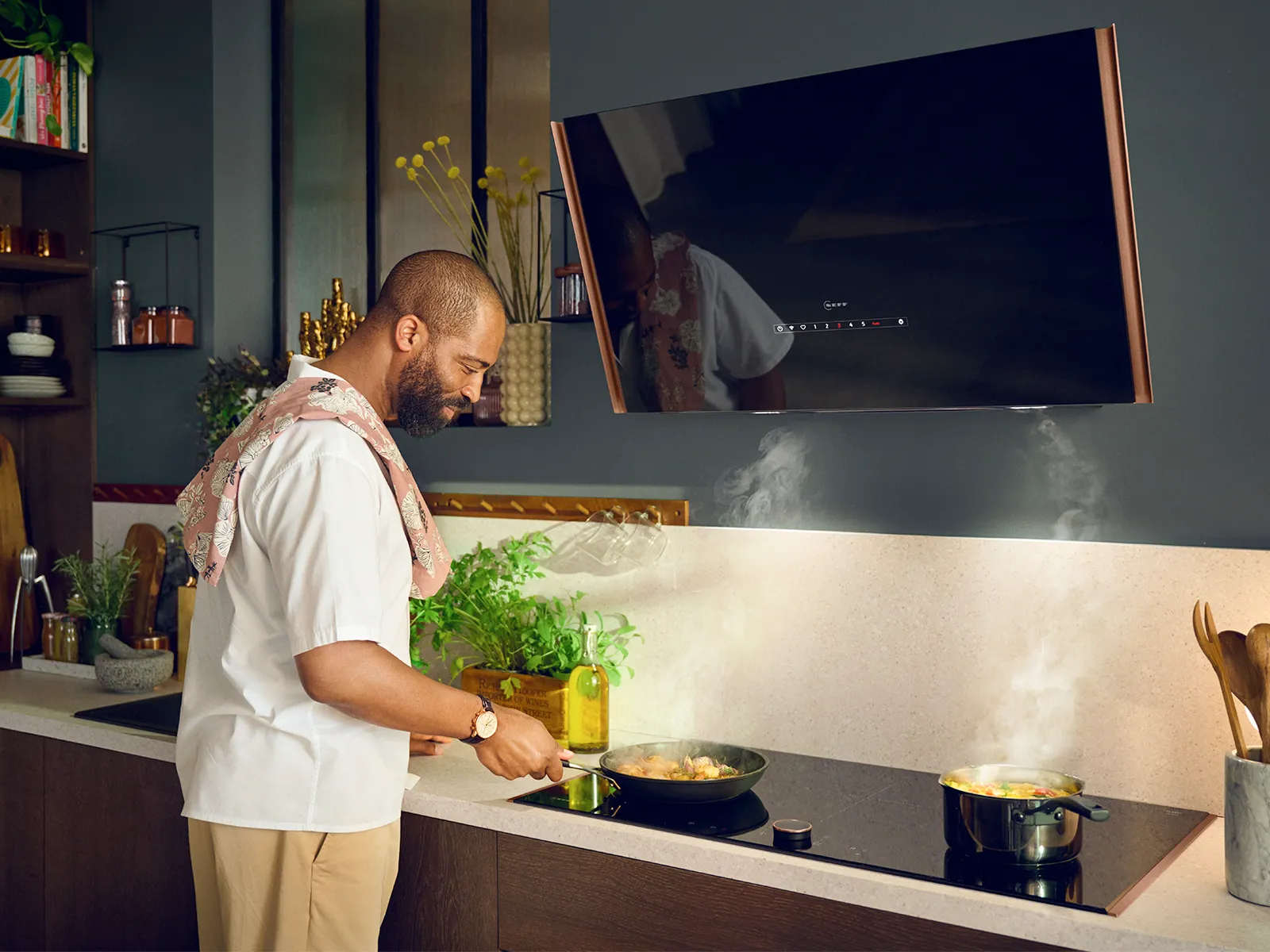 Man Kochen Lebensmittel auf Herd in Küche mit großem TV-Bildschirm im Hintergrund.