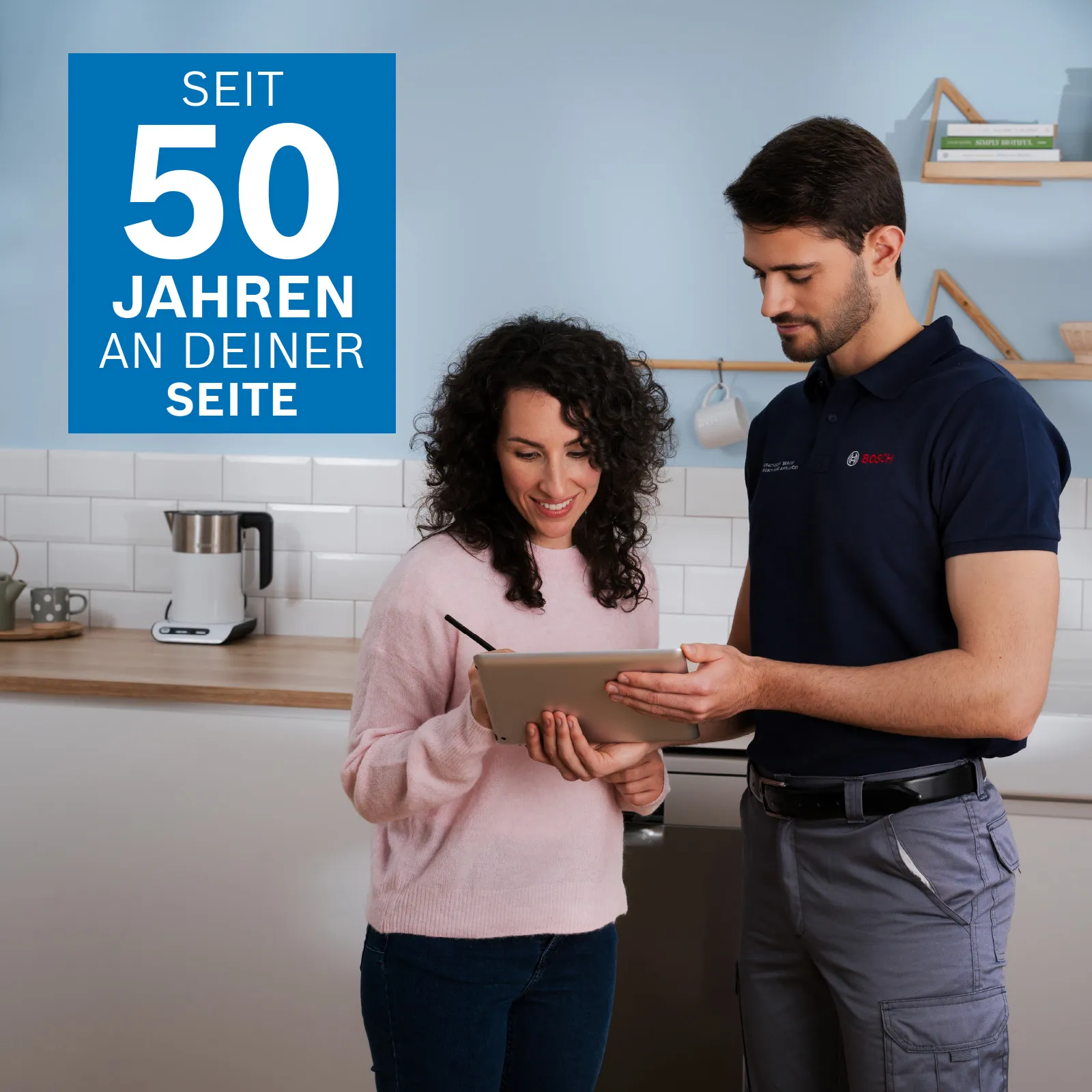 Ein Bosch Techniker mit Handschuhen repariert ein Gerät in einer modernen Küche. Eine Frau beobachtet ihn aufmerksam. Werkzeuge liegen daneben auf der Arbeitsplatte.