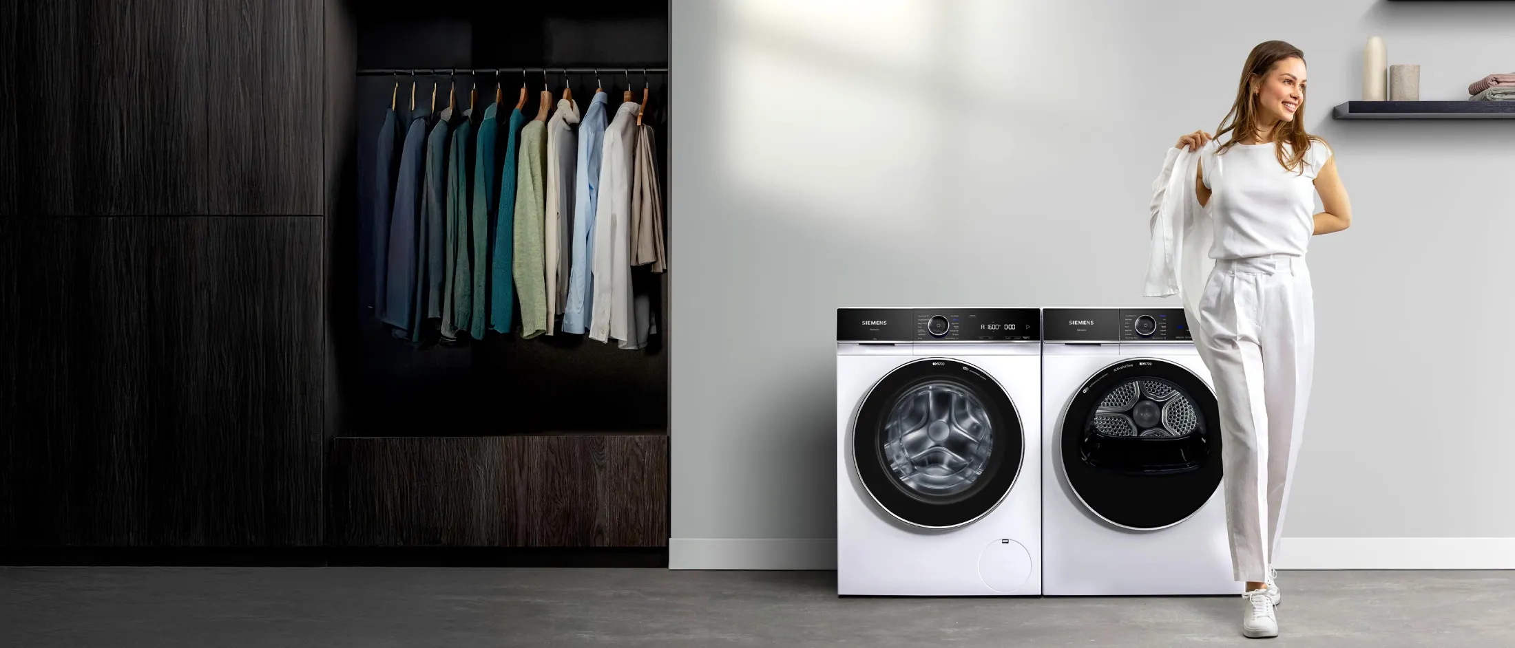 Una joven se pone un blazer en un cuarto de lavado equipado con una lavadora y una secadora iQ700 de Siemens.