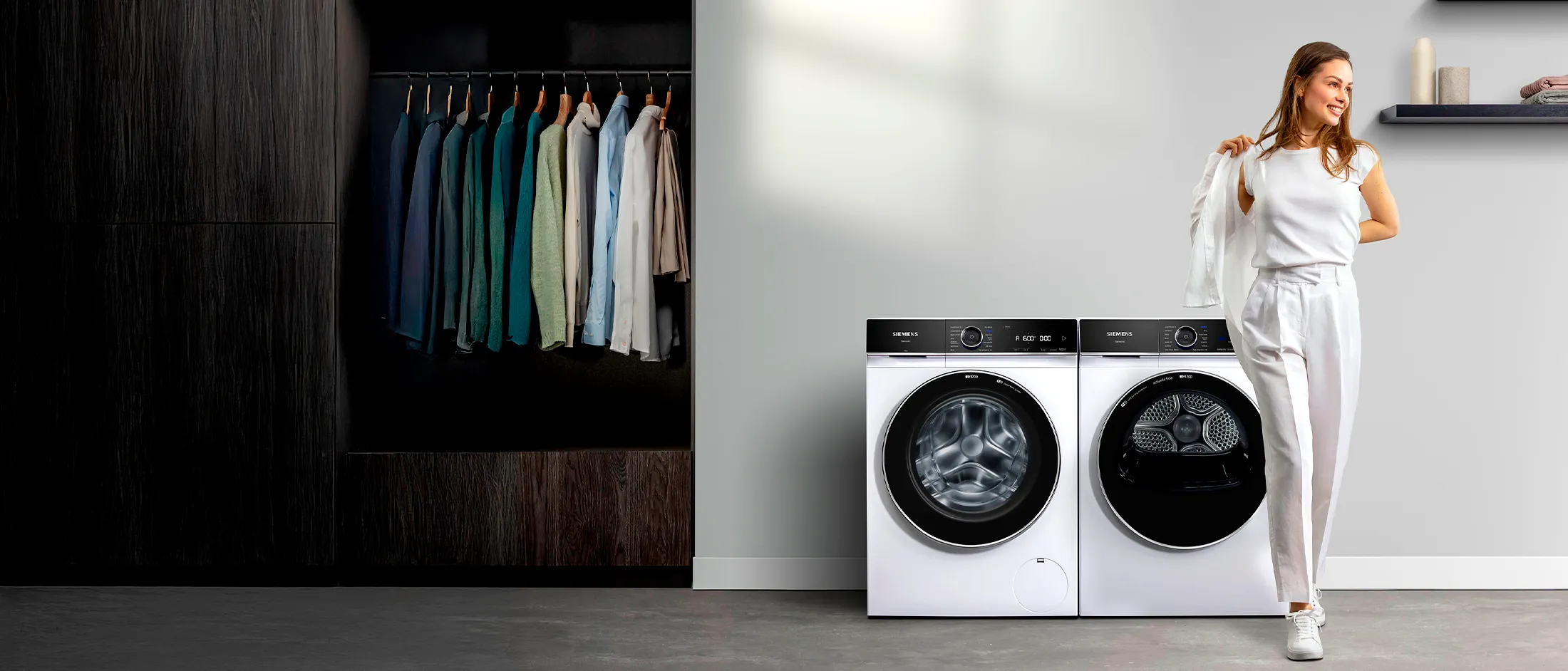 Una joven se pone un blazer en un cuarto de lavado equipado con una lavadora y una secadora iQ700 de Siemens.