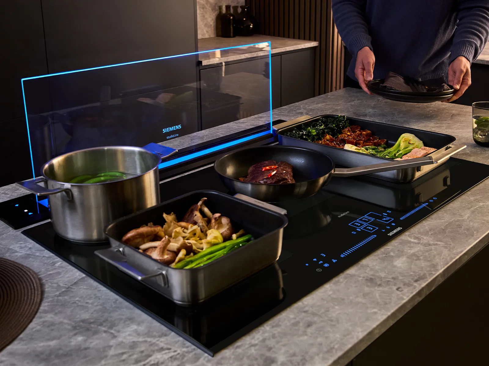 A modern kitchen scene showing a sleek black Siemens induction cooktop integrated into a marble-patterned countertop. 