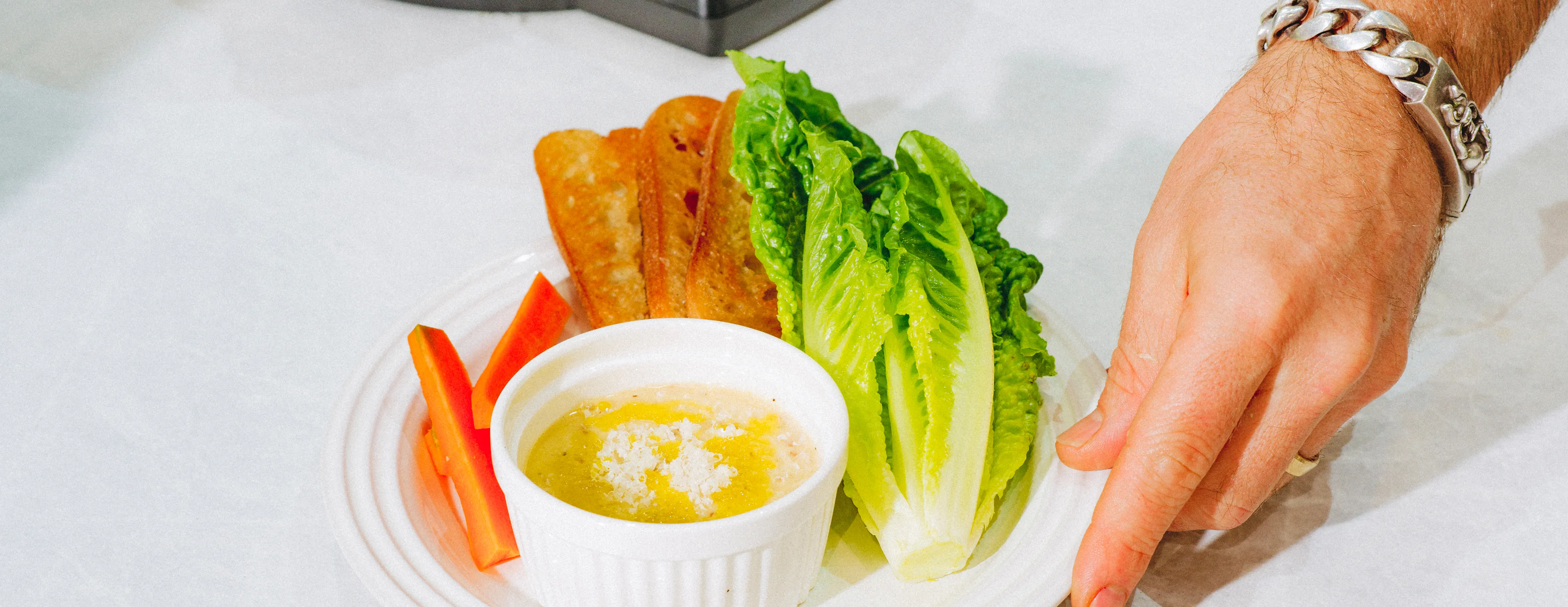 Plate with lettuce, bread slices, red pepper sticks, and dipping sauce, hand holding it.