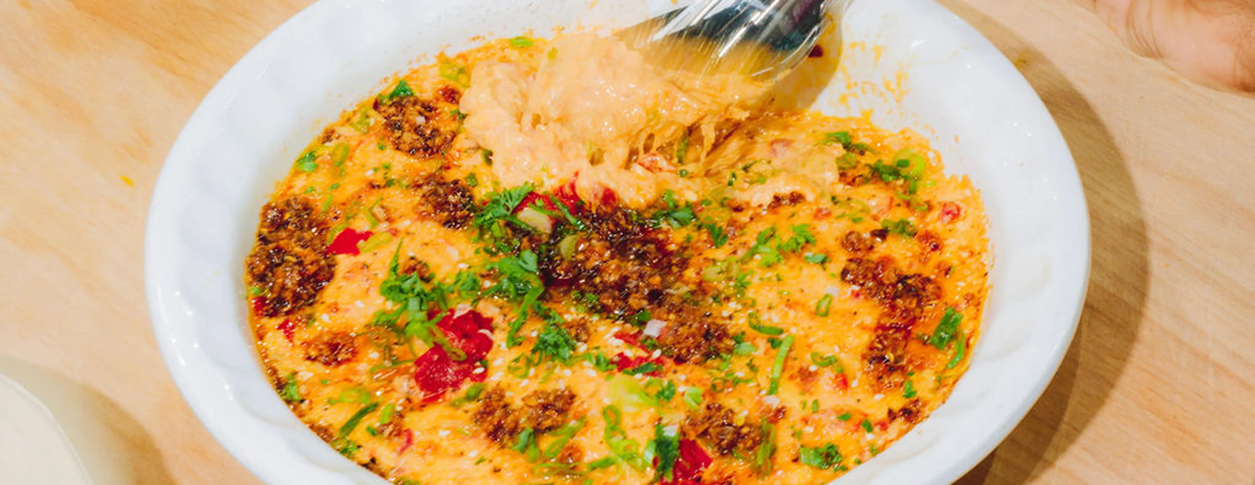 Gochujang Pimento dish filled with baked dish topped with herbs and spices on a wooden board.