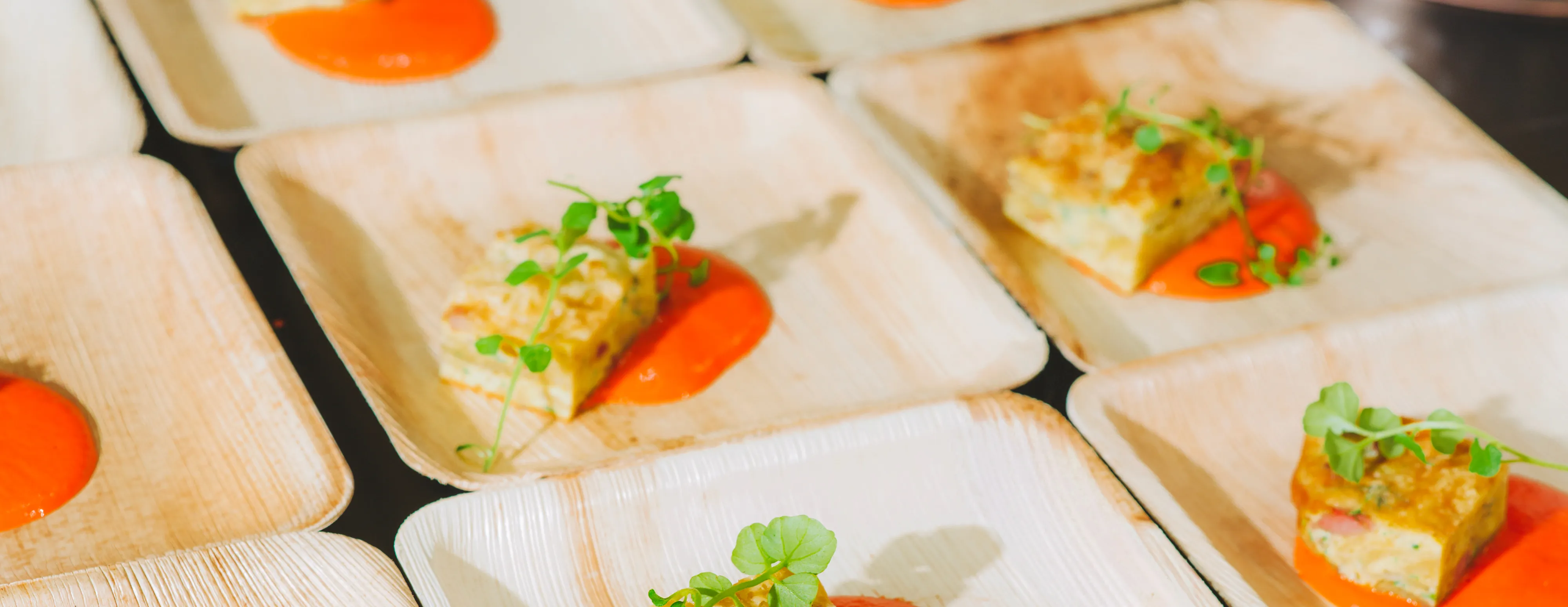 Appetizers served on square plates with a red sauce base and garnished with greens.
