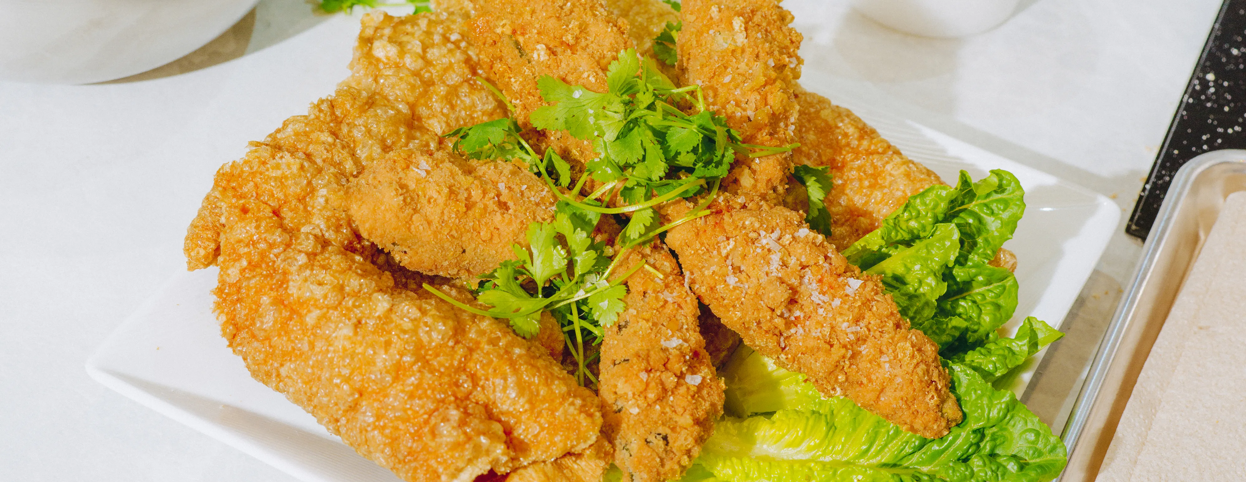Fried Jalapeno poppers on a white square plate garnished with lettuce and herbs, served on a table.
